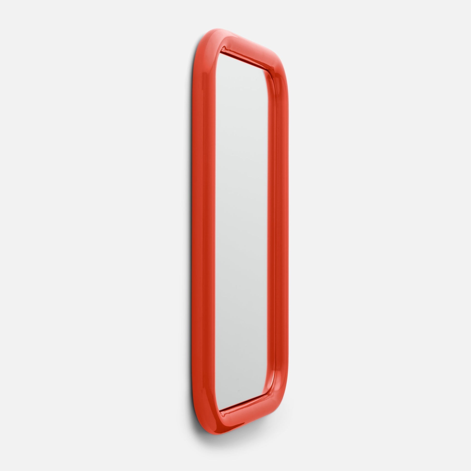 Angled side view of Forma Mirror showcasing glossy rounded red frame on pale gray background