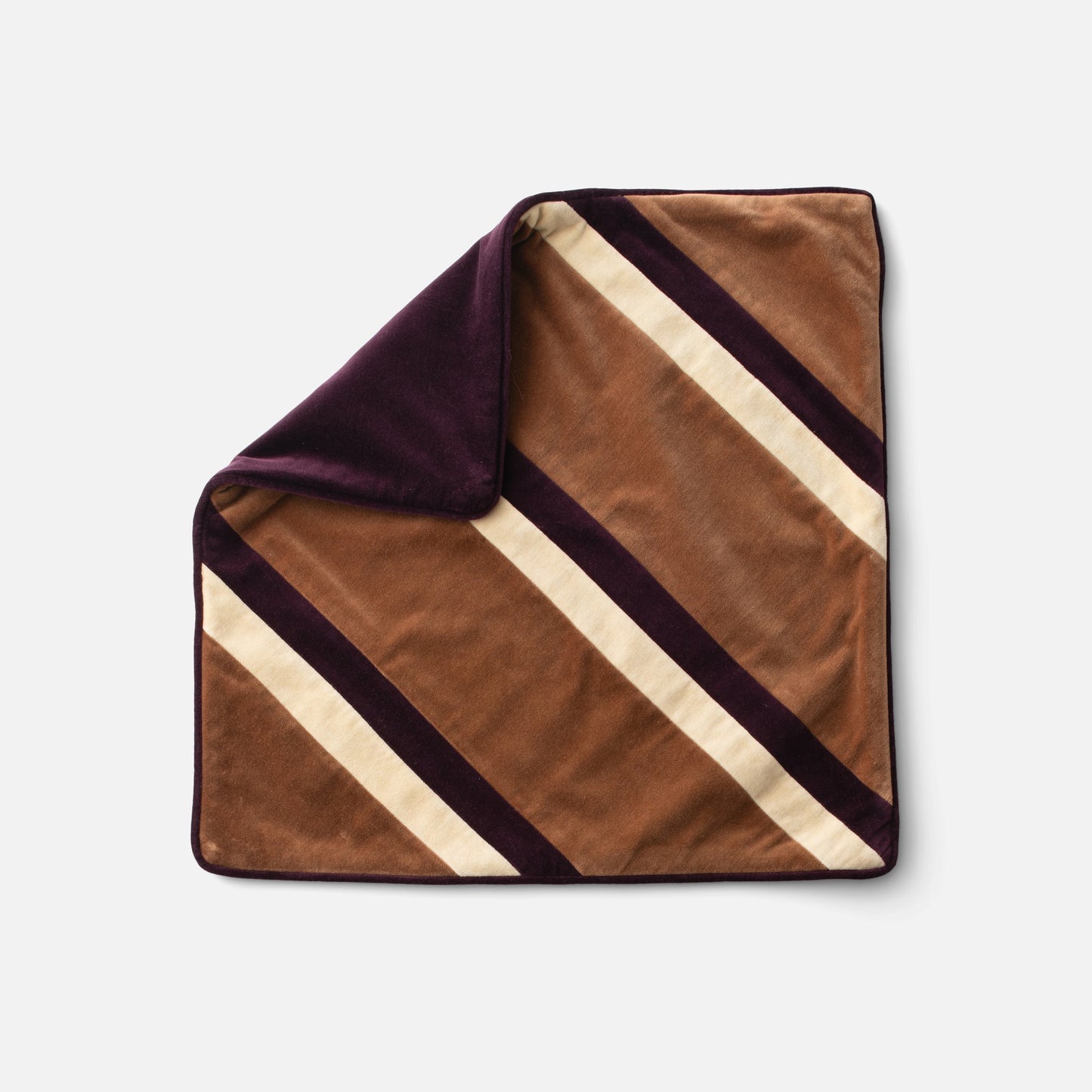 Flat lay of Pieced Velvet Pillow Cover showing diagonal rugby stripes and folded corner revealing plum velvet back on white