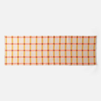 Flat lay of Plaid Wool Reversible Rug showcasing peach, mustard, and rust plaid on a white background