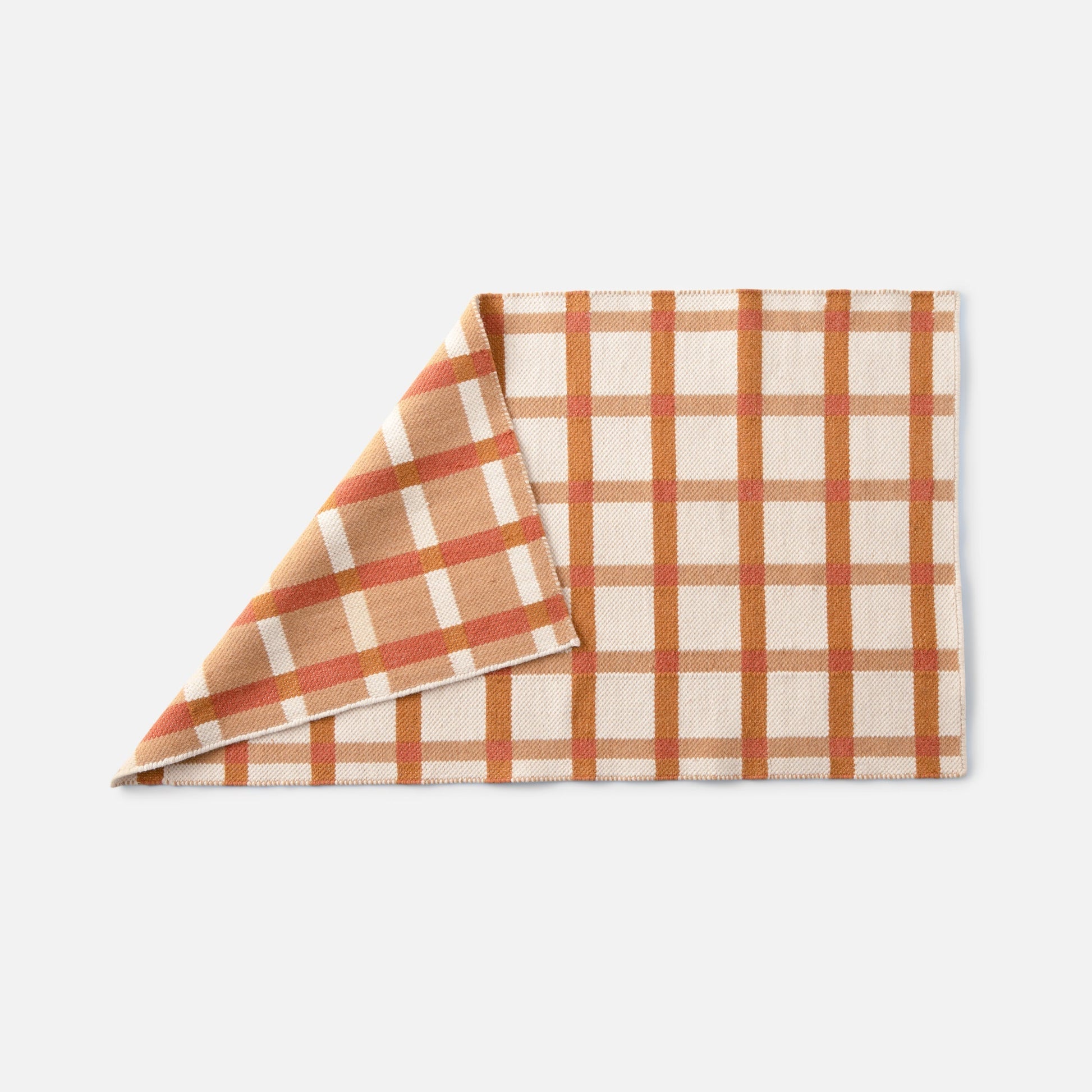 Folded corner view of Plaid Wool Reversible Rug showing reversible weave and tan, cream, and rust plaid on a white background