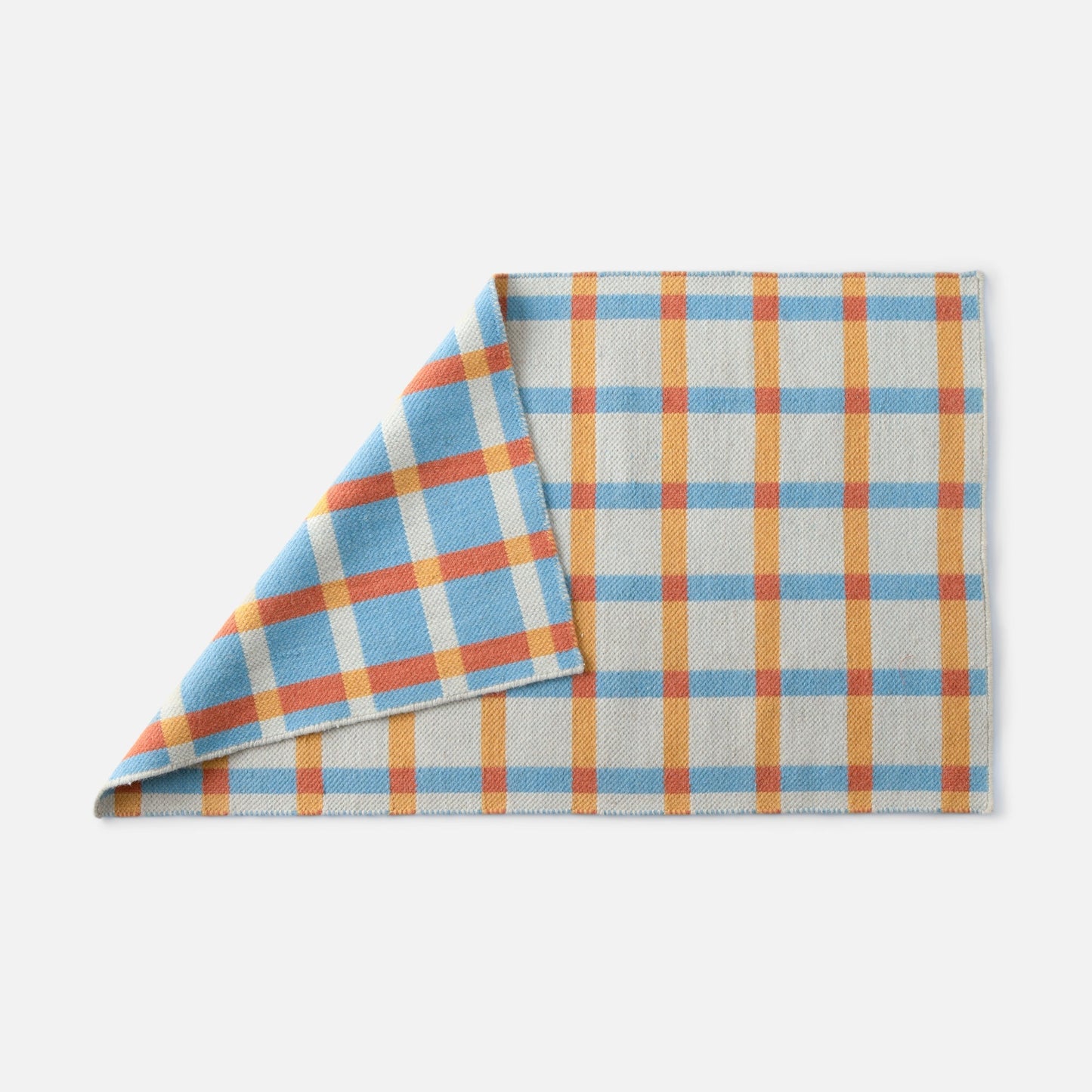 Corner of Plaid Wool Reversible Rug showing folded edge and reversible blue, orange, yellow plaid on white background