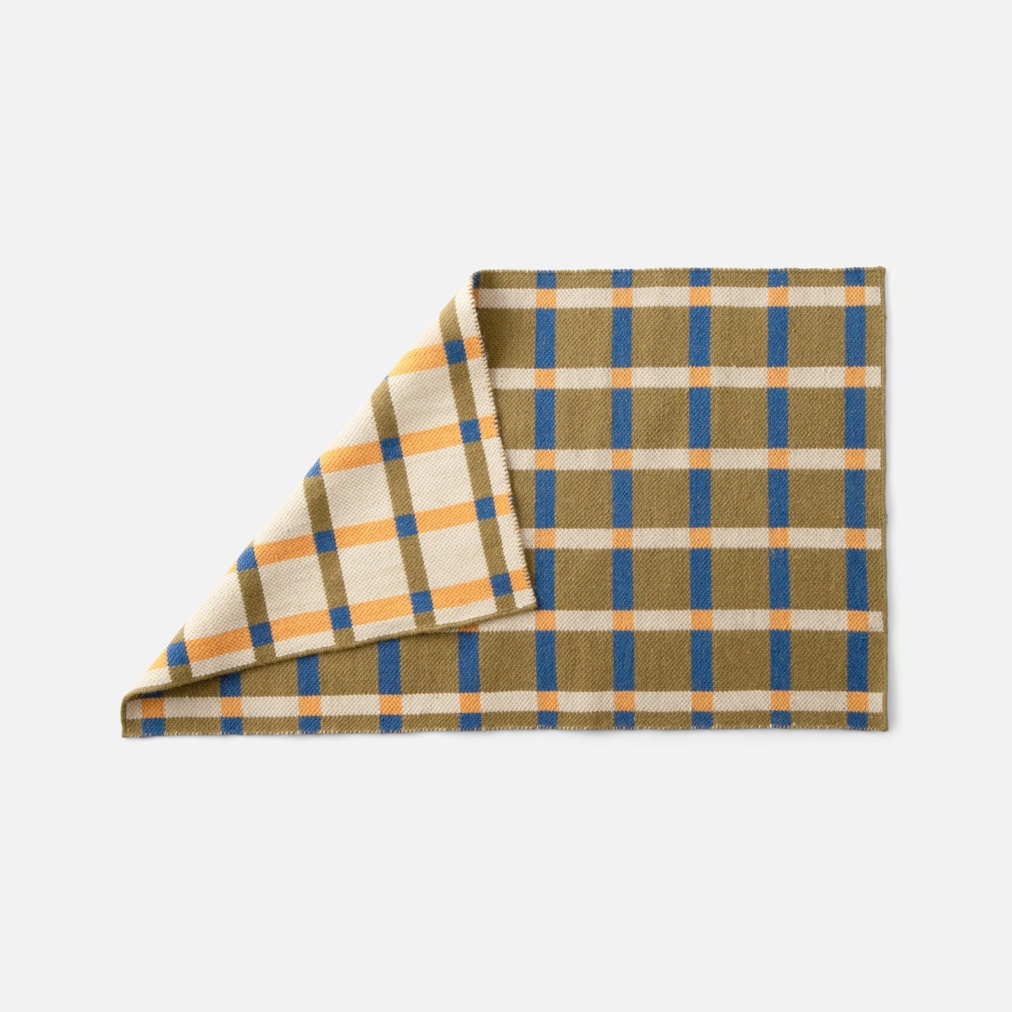 Angled close up of Plaid Wool Reversible Rug showcasing reversible weave and plaid pattern in olive, blue, orange and cream on a white background