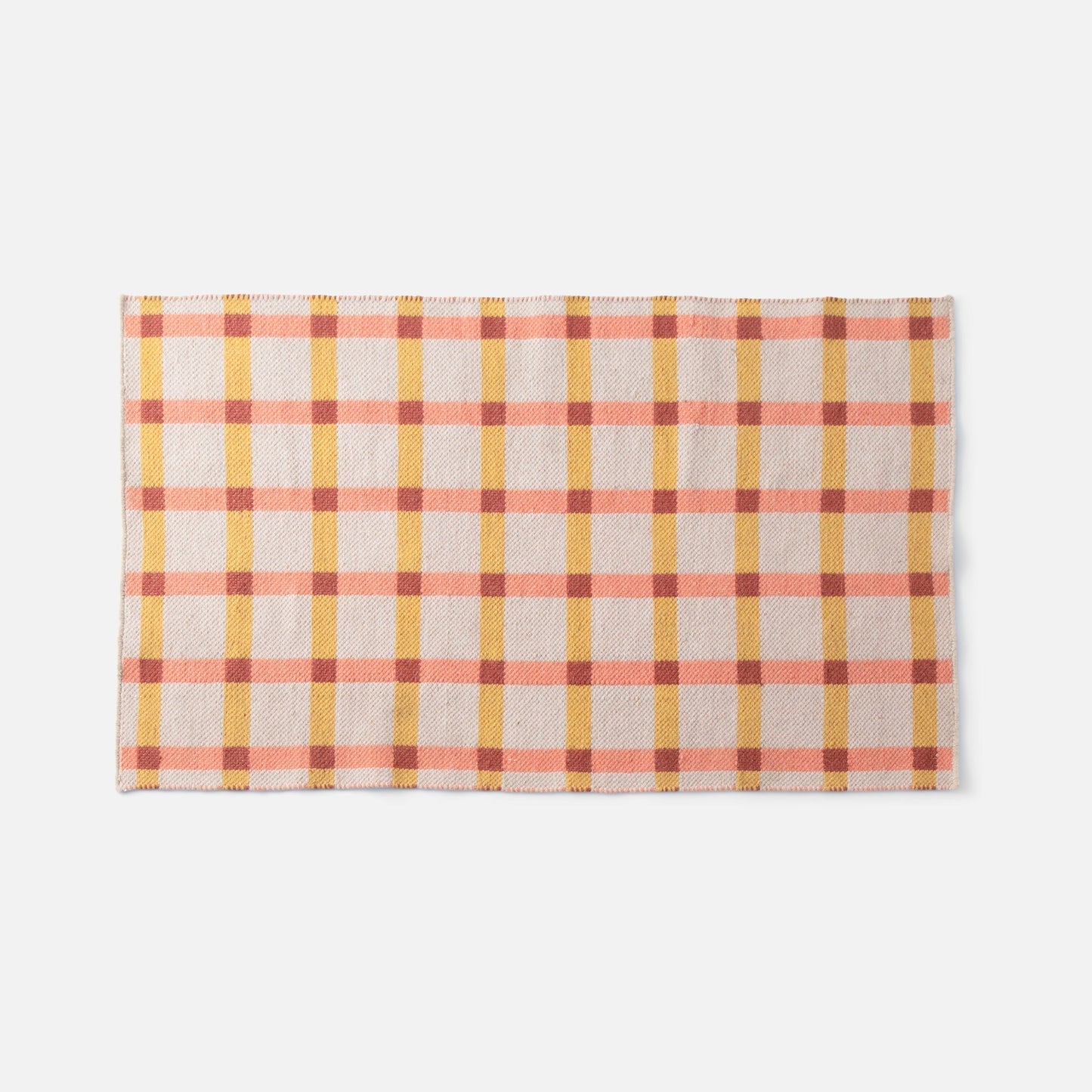 Cropped top view of Plaid Wool Reversible Rug showcasing its reversible weave and pink, yellow, and rust plaid on white background
