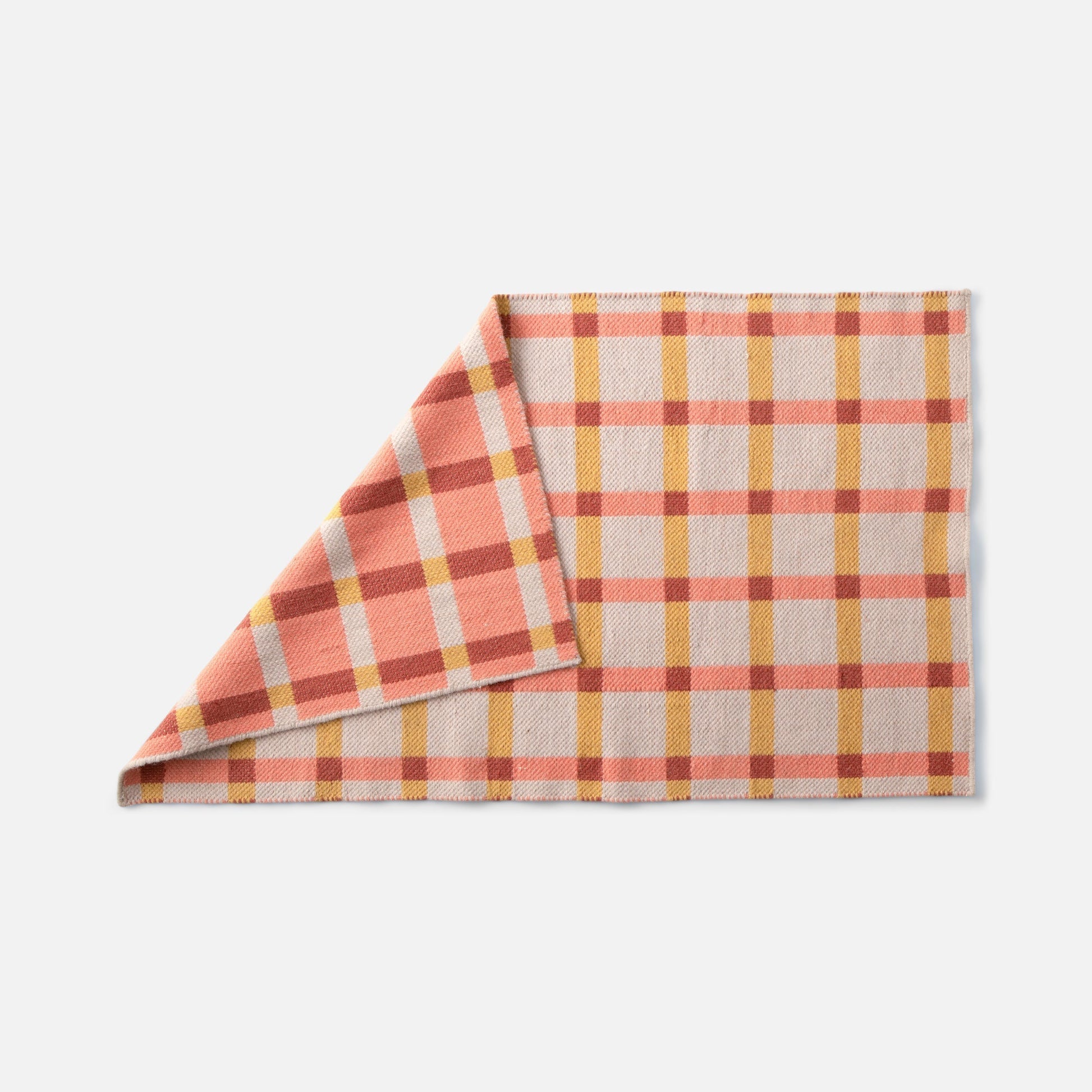 Folded corner view of Plaid Wool Reversible Rug showing reversible weave and coral, yellow, and rust plaid on white background