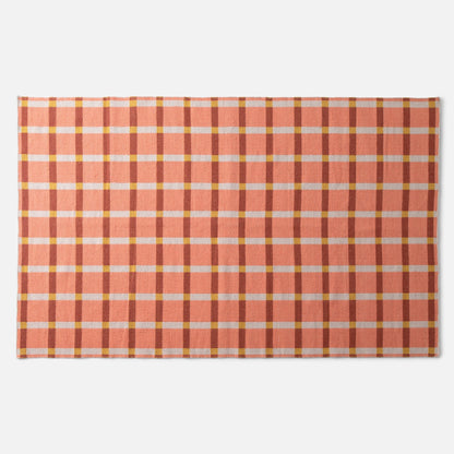 Top-down view of Plaid Wool Reversible Rug showcasing peach-and-rust plaid with white and yellow checks on a white background