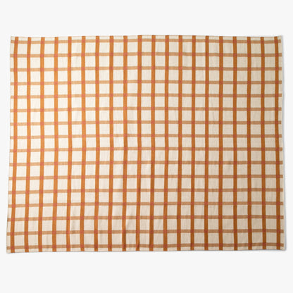Top-down view of Plaid Wool Reversible Rug showcasing warm orange and tan plaid and woven wool texture on white background
