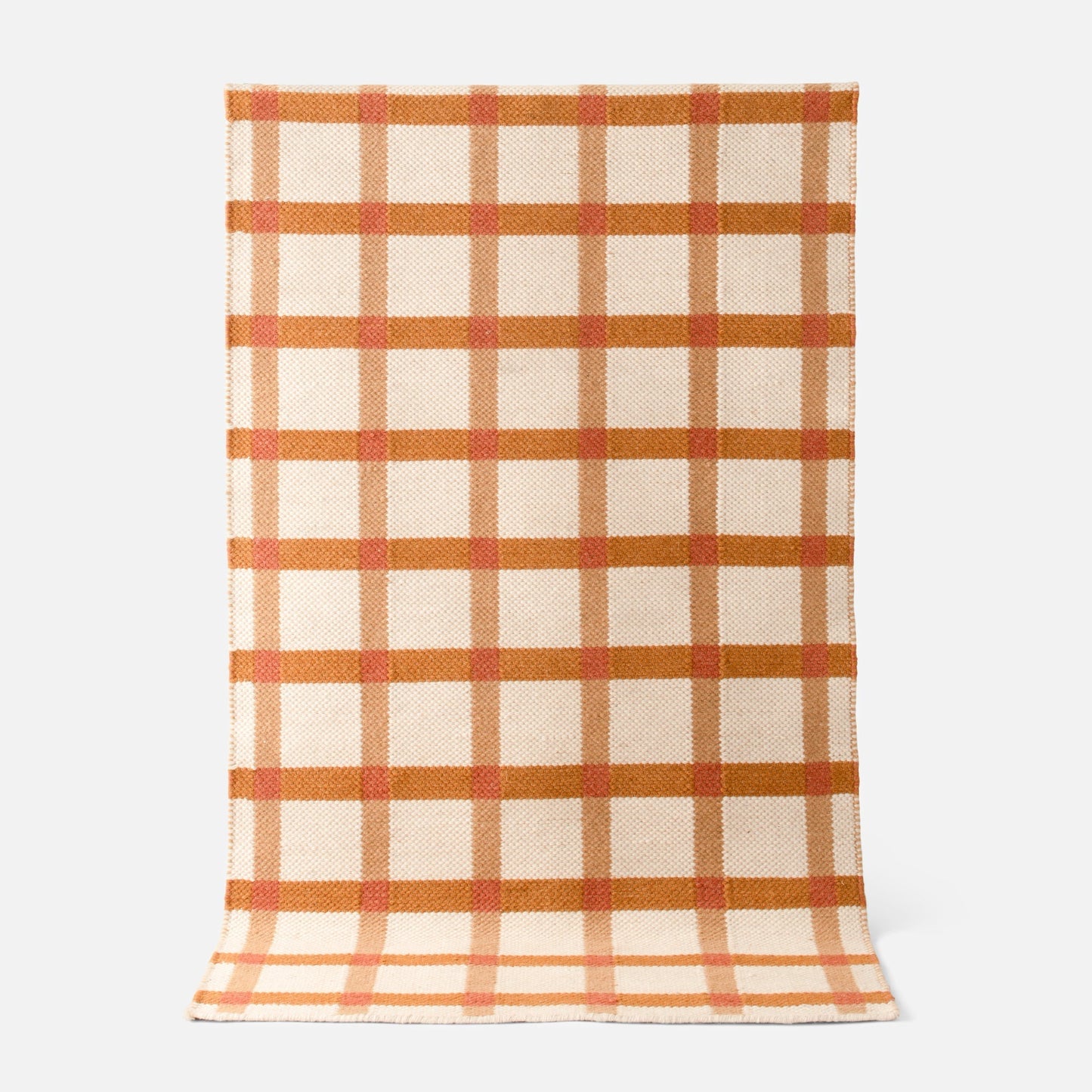 Top-down view of Plaid Wool Reversible Rug showcasing cream wool with rust orange and tan plaid and handwoven reversible texture on light gray background