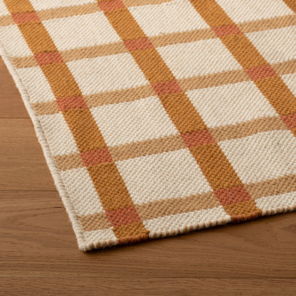 Angled close-up of Plaid Wool Reversible Rug showcasing handwoven natural-dyed wool plaid in cream, tan, mustard, and rust on a wood floor