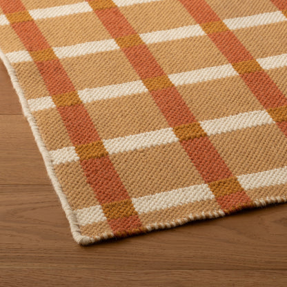 Close-up of Plaid Wool Reversible Rug showing handwoven texture, tan/cream/rust plaid and finished edge on wood floor