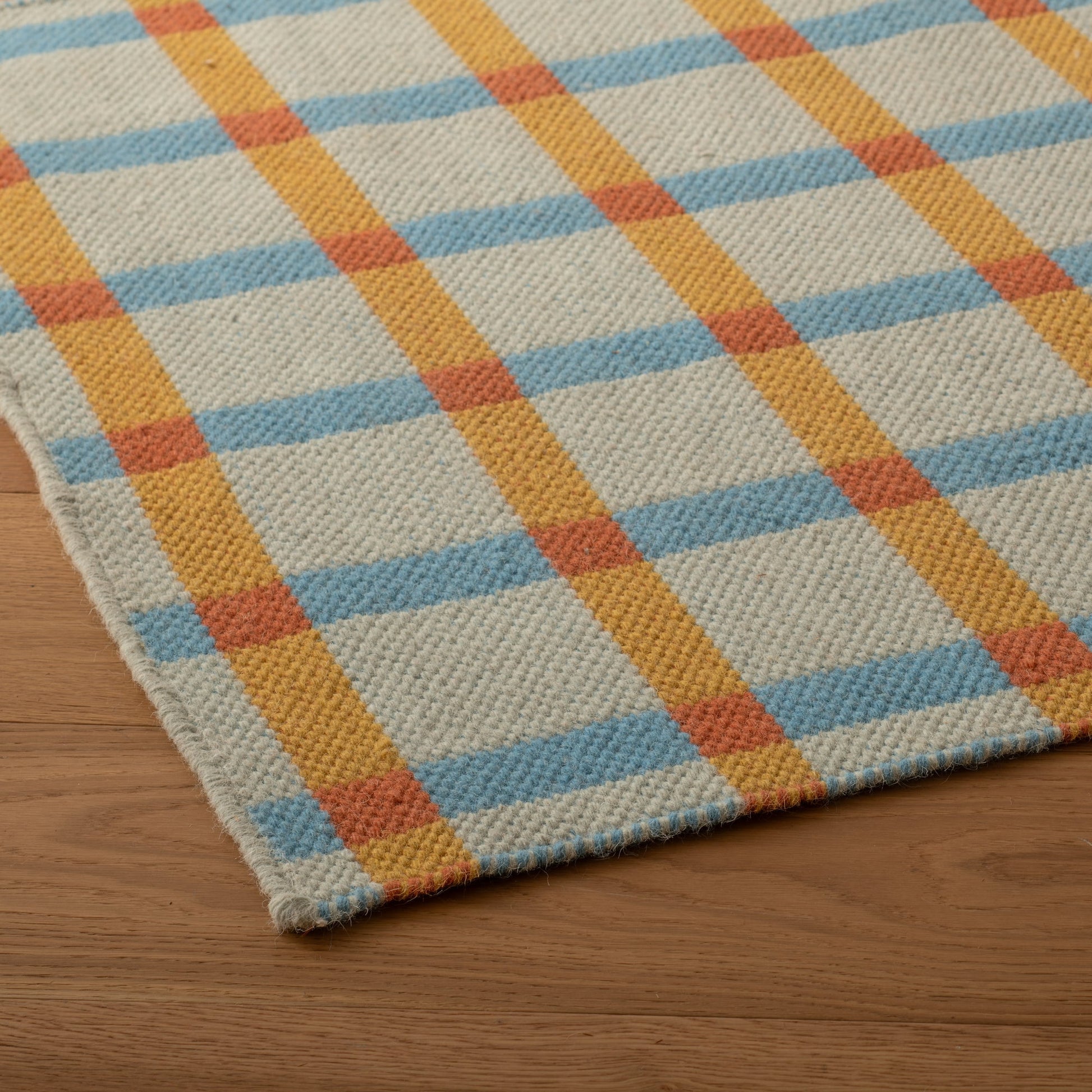 Angled close-up of Plaid Wool Reversible Rug showing handwoven texture and blue, mustard and rust plaid on a wood floor