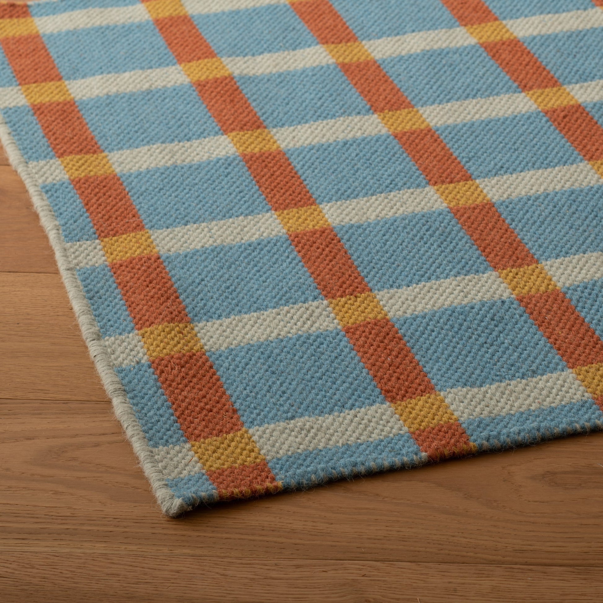 Close-up of Plaid Wool Reversible Rug showcasing handwoven wool texture and blue, cream, rust and yellow plaid on wood floor