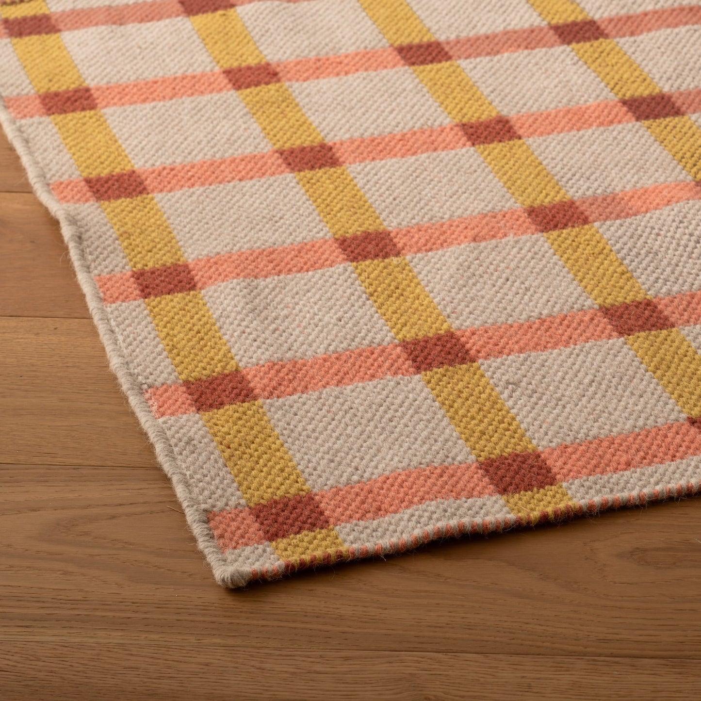 Angled close-up of Plaid Wool Reversible Rug showing handwoven wool plaid in peach and mustard on hardwood floor