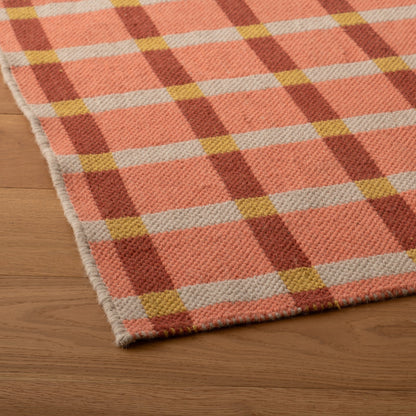 Close-up of Plaid Wool Reversible Rug corner showing handwoven plaid in pink, rust, cream and mustard on wood floor