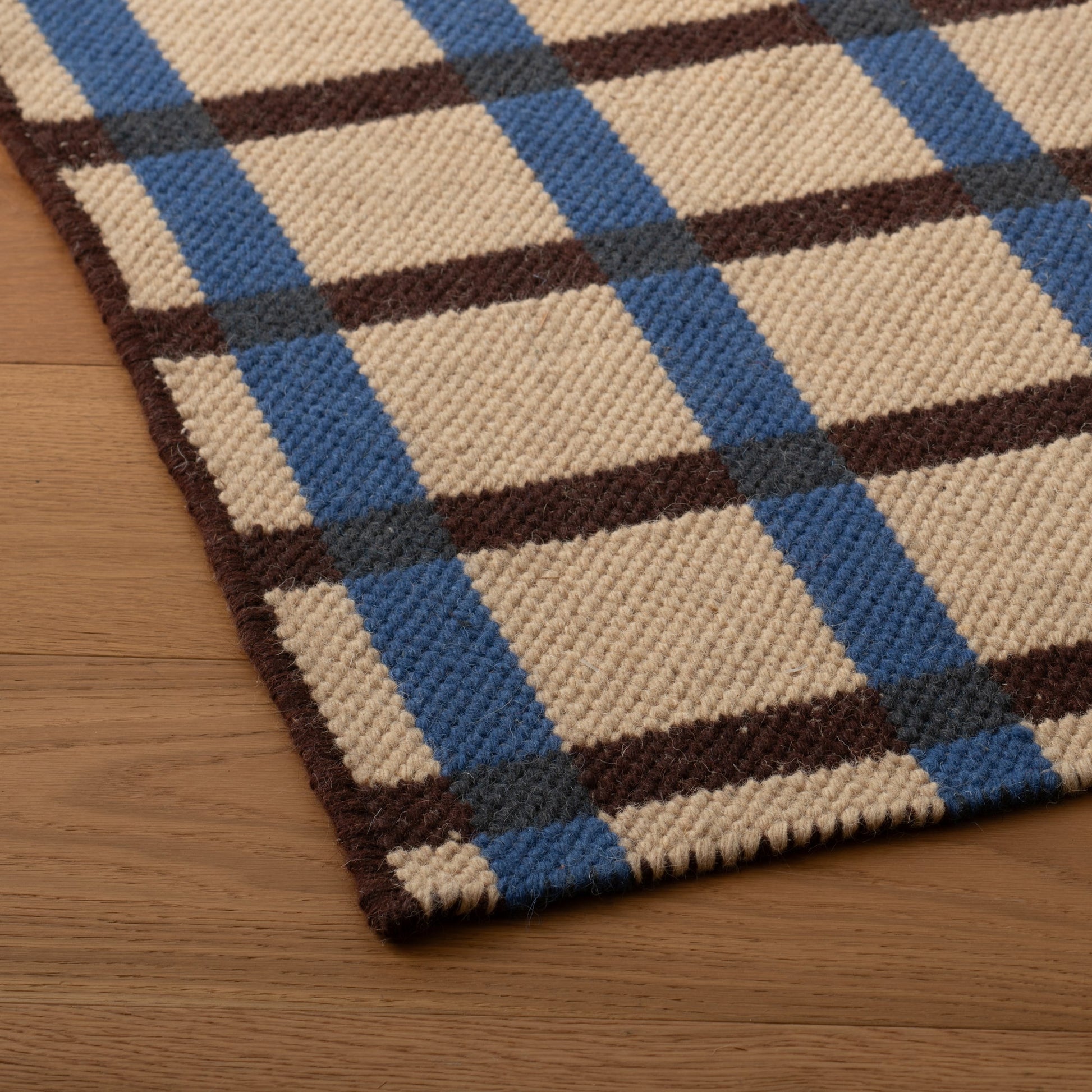 Close-up of Plaid Wool Reversible Rug showing handwoven wool texture and blue-and-brown plaid on wood floor