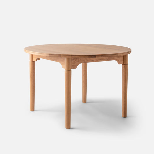 Three-quarter view of Willard Dining Table showcasing round solid oak top, tapered legs, and apron on white background
