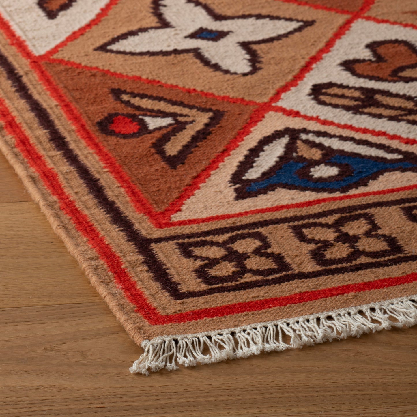 Close-up of Linnea Wool Flatweave Rug showcasing hand-drawn floral motifs, flatweave texture, and fringe on a wood floor