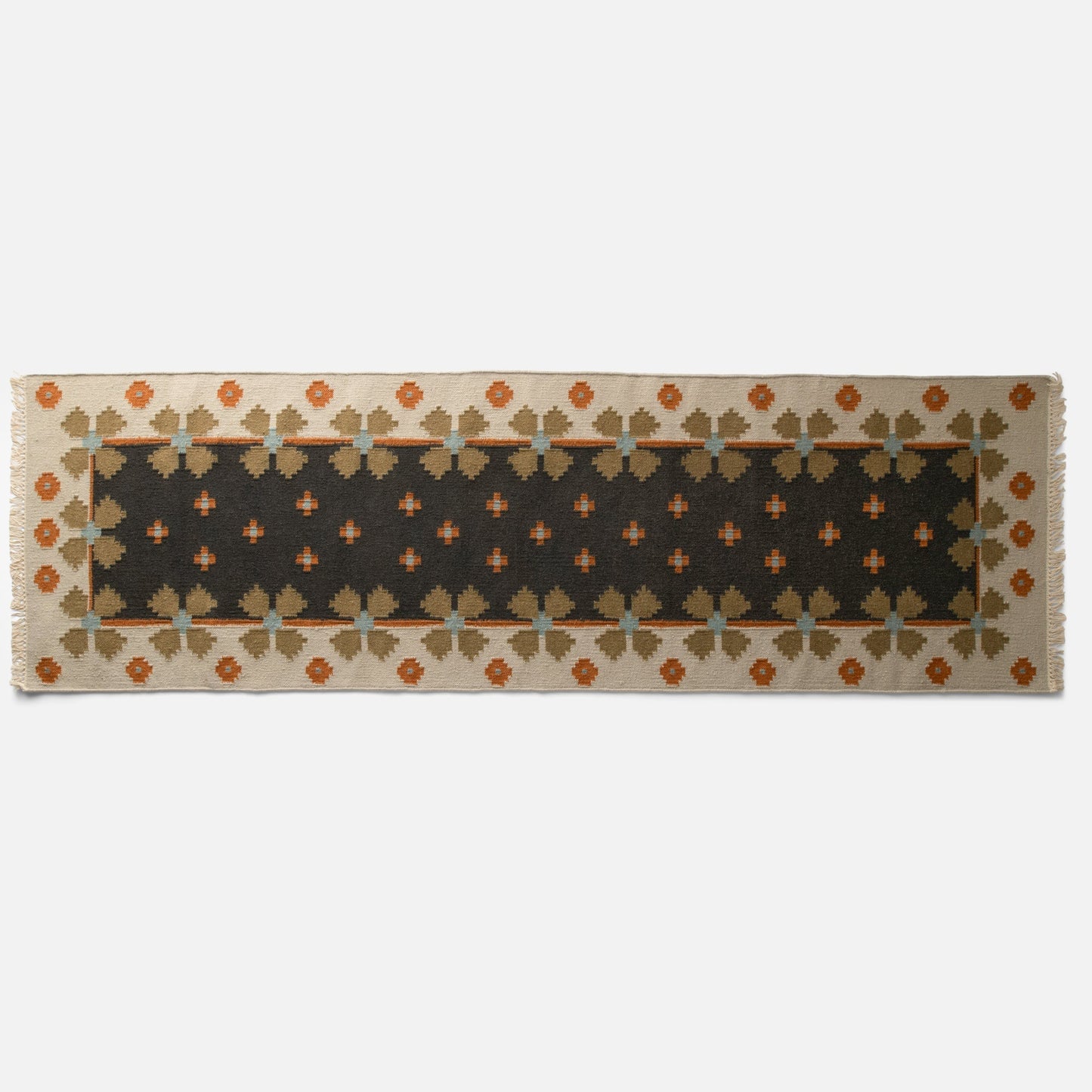 Partial top view of Flora Wool Flatweave Rug showing folk floral pattern in black, cream, orange and tan with fringed edge on white background