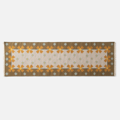 Top-down view of Flora Wool Flatweave Rug showcasing mustard floral border and blue dot motifs on a beige field with white background
