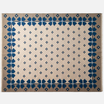 Top-down view of Flora Wool Flatweave Rug showcasing blue floral border and small navy cross motifs on a beige field