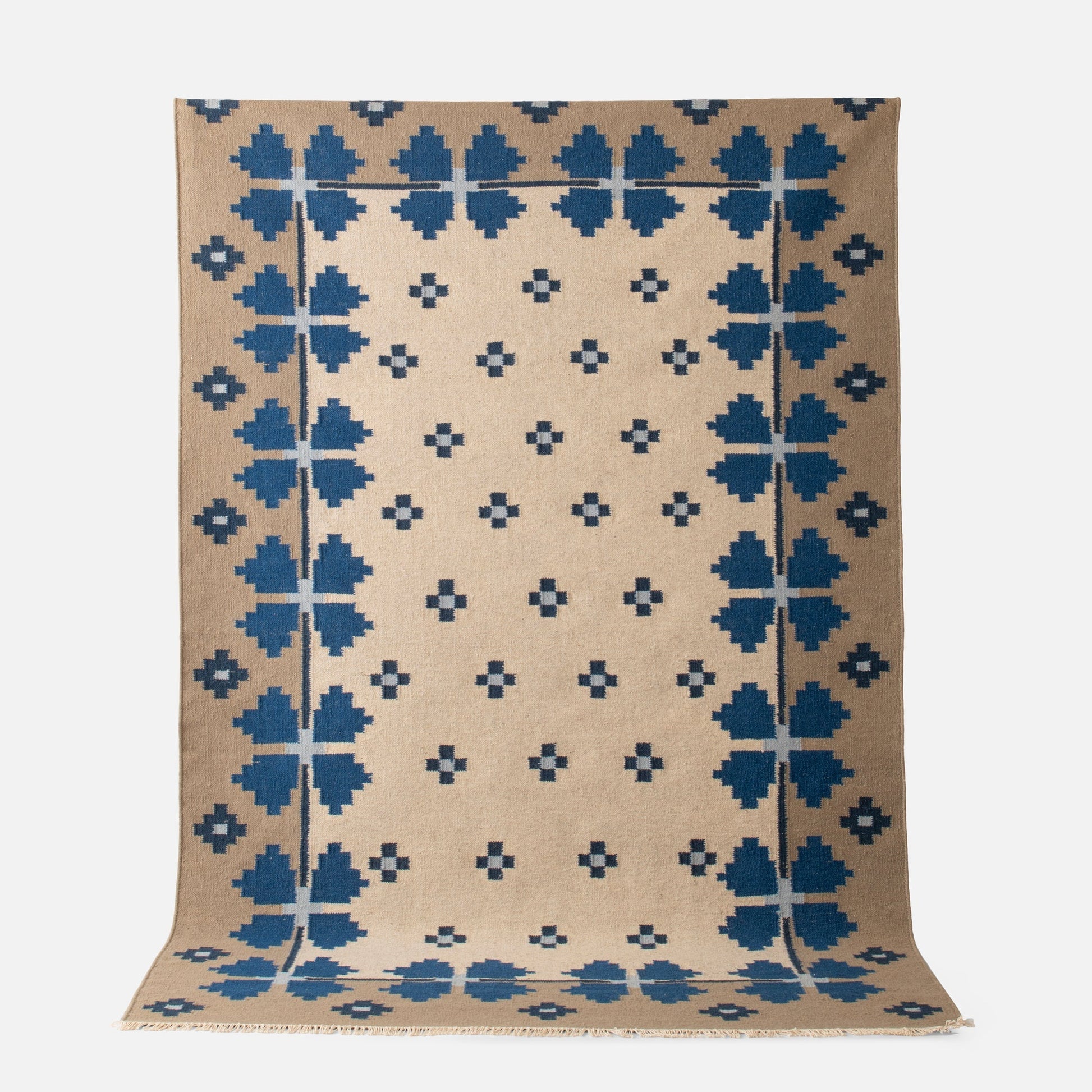 Partial top view of Flora Wool Flatweave Rug showing blue folk floral pattern on tan wool background