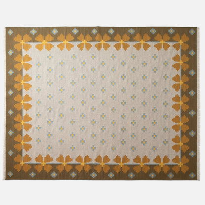 Top-down view of Flora Wool Flatweave Rug showing mustard floral border and small blue-and-yellow motifs on a beige field