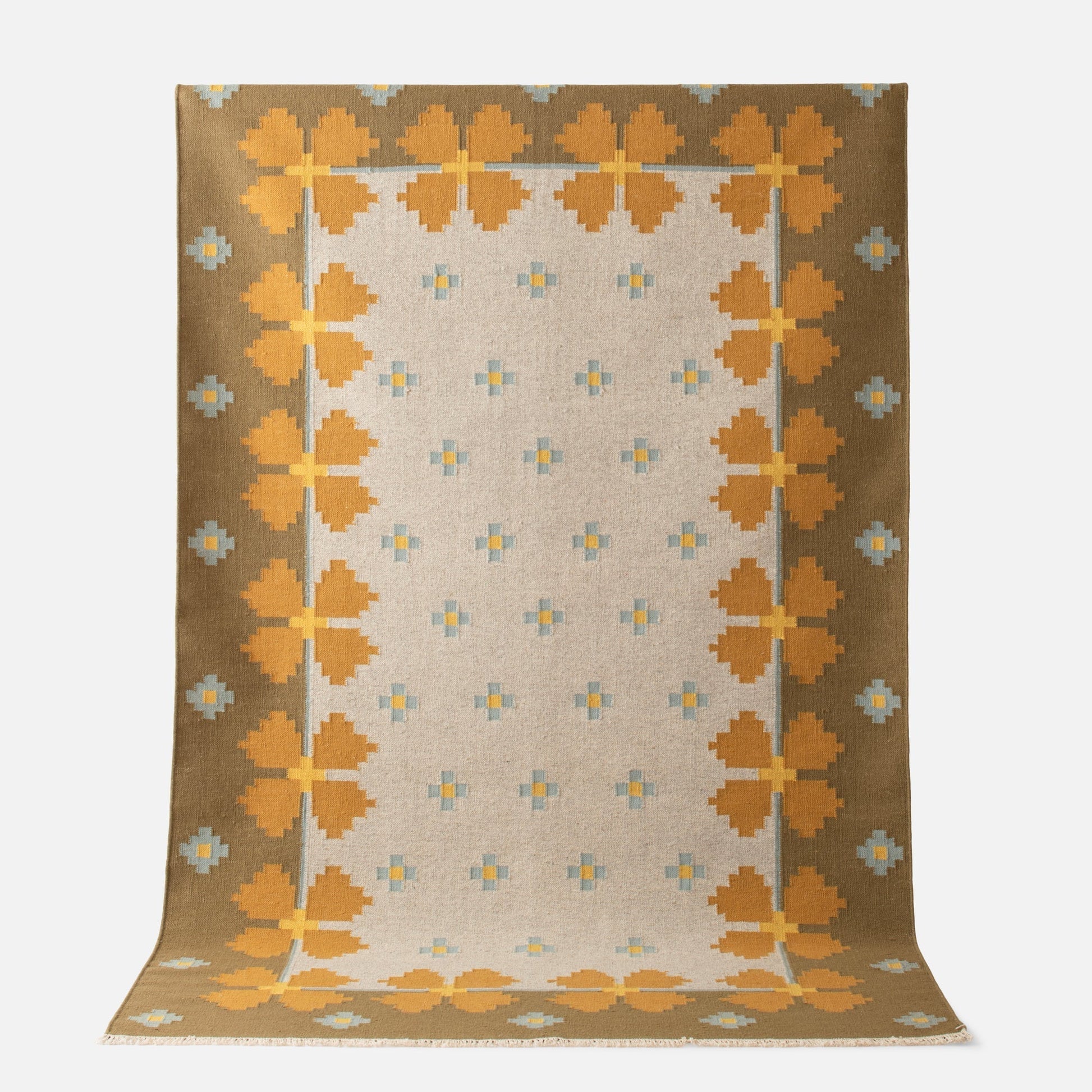 Angled top-down view of Flora Wool Flatweave Rug showcasing golden yellow floral border and small blue cross motifs on a beige field with white background