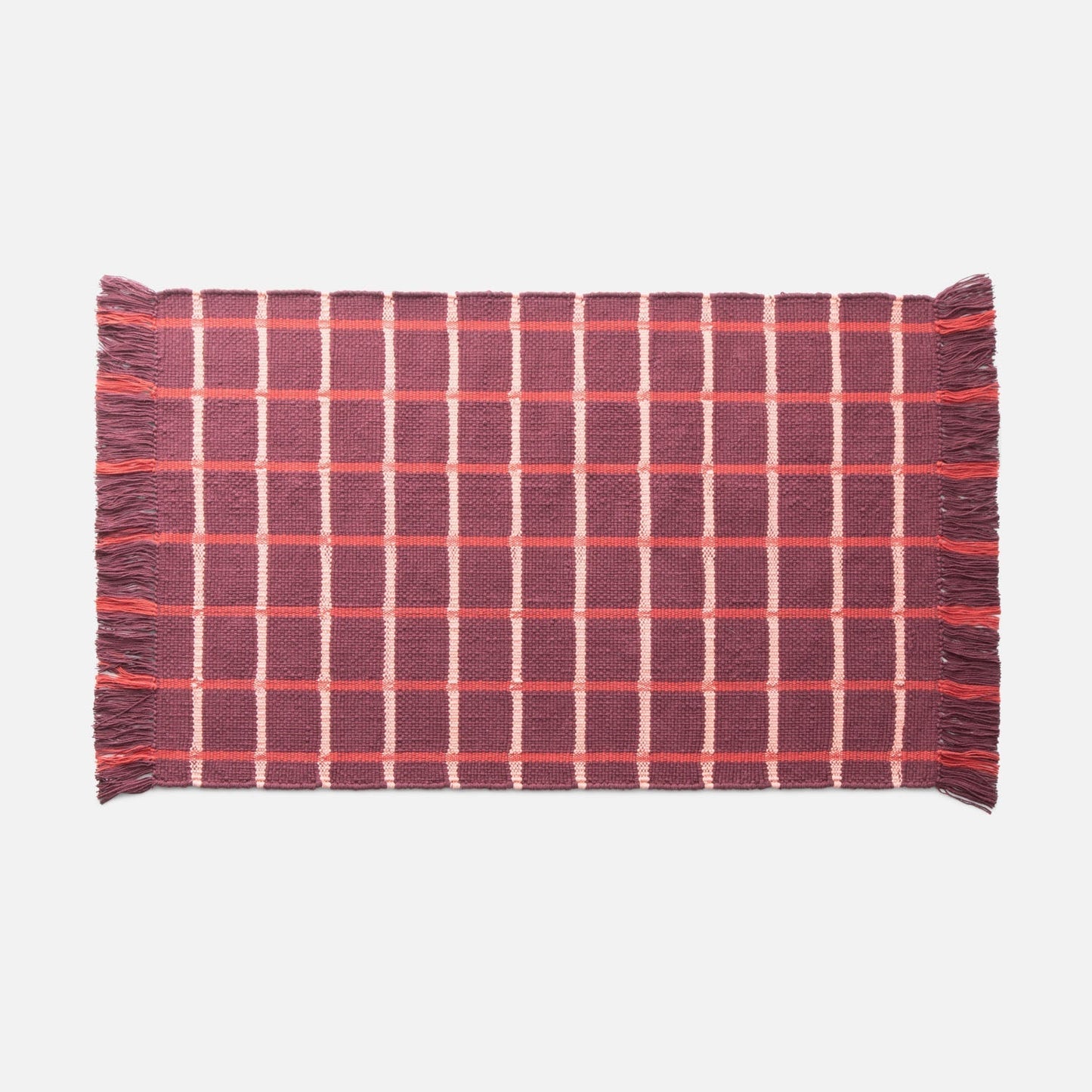 Flat lay of Cotton Grid Flatweave Rug showing red and pink grid pattern and fringed ends on pale gray background
