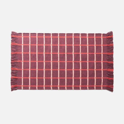 Flat lay of Cotton Grid Flatweave Rug showing red and pink grid pattern and fringed ends on pale gray background