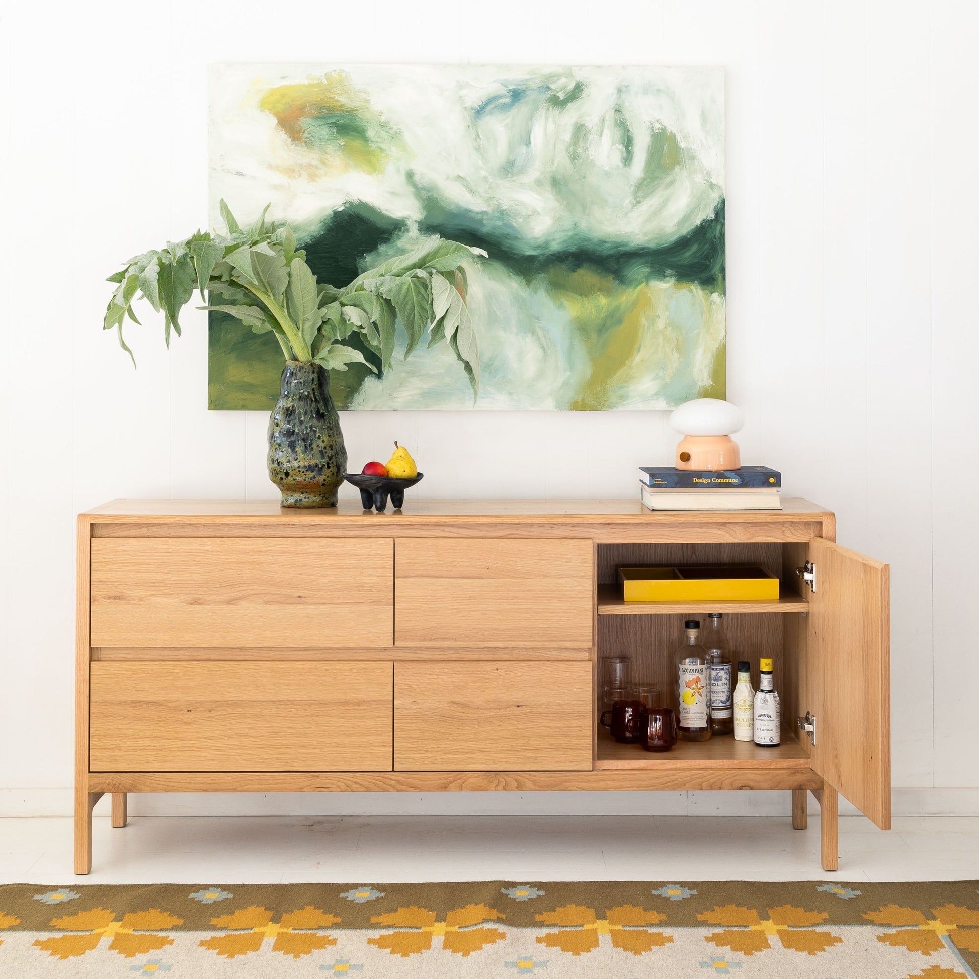 Flora Wool Flatweave Rug shown under a wooden console styled with a green vase of leaves, a small fruit bowl, and stacked books