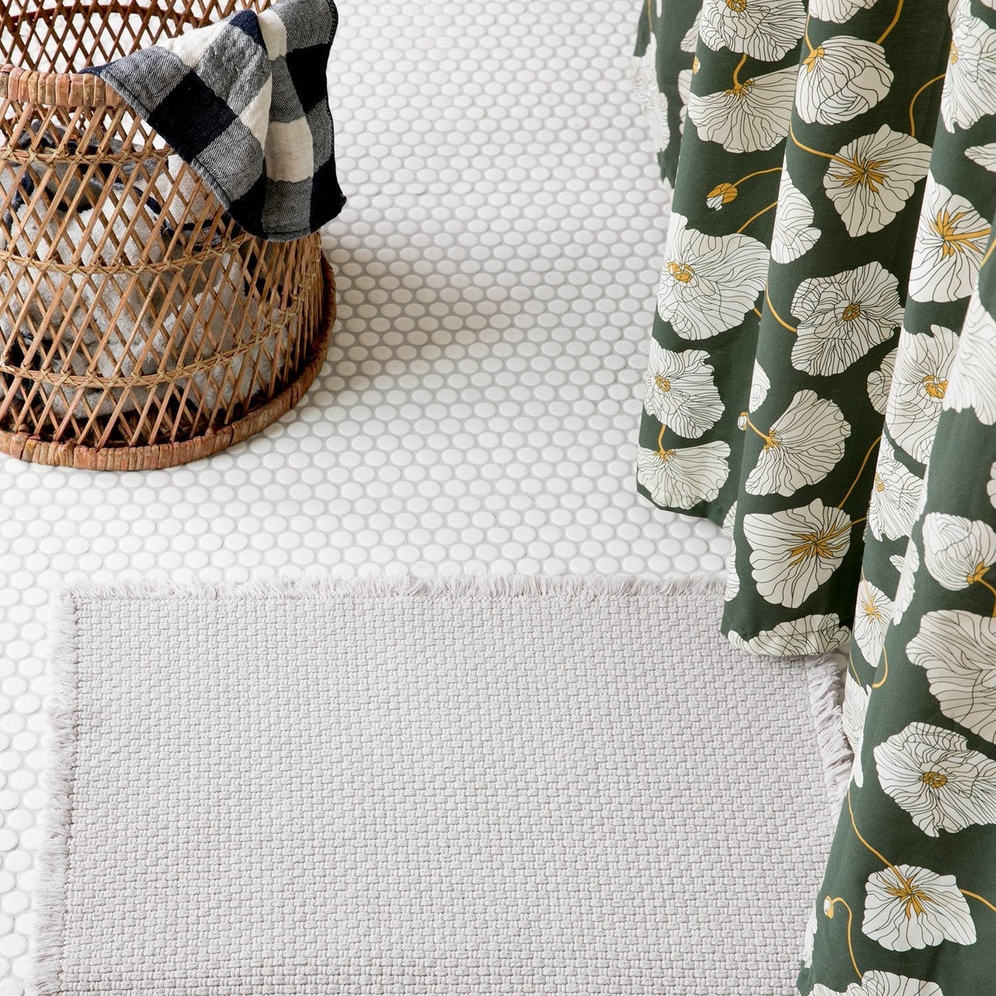 Close-up of Blooming Field shower curtain showing white poppies on green with wicker basket and penny-tile floor