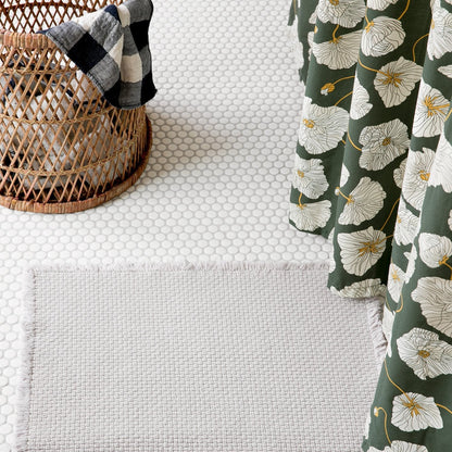 Close-up of Blooming Field shower curtain showing white poppies on green with wicker basket and penny-tile floor