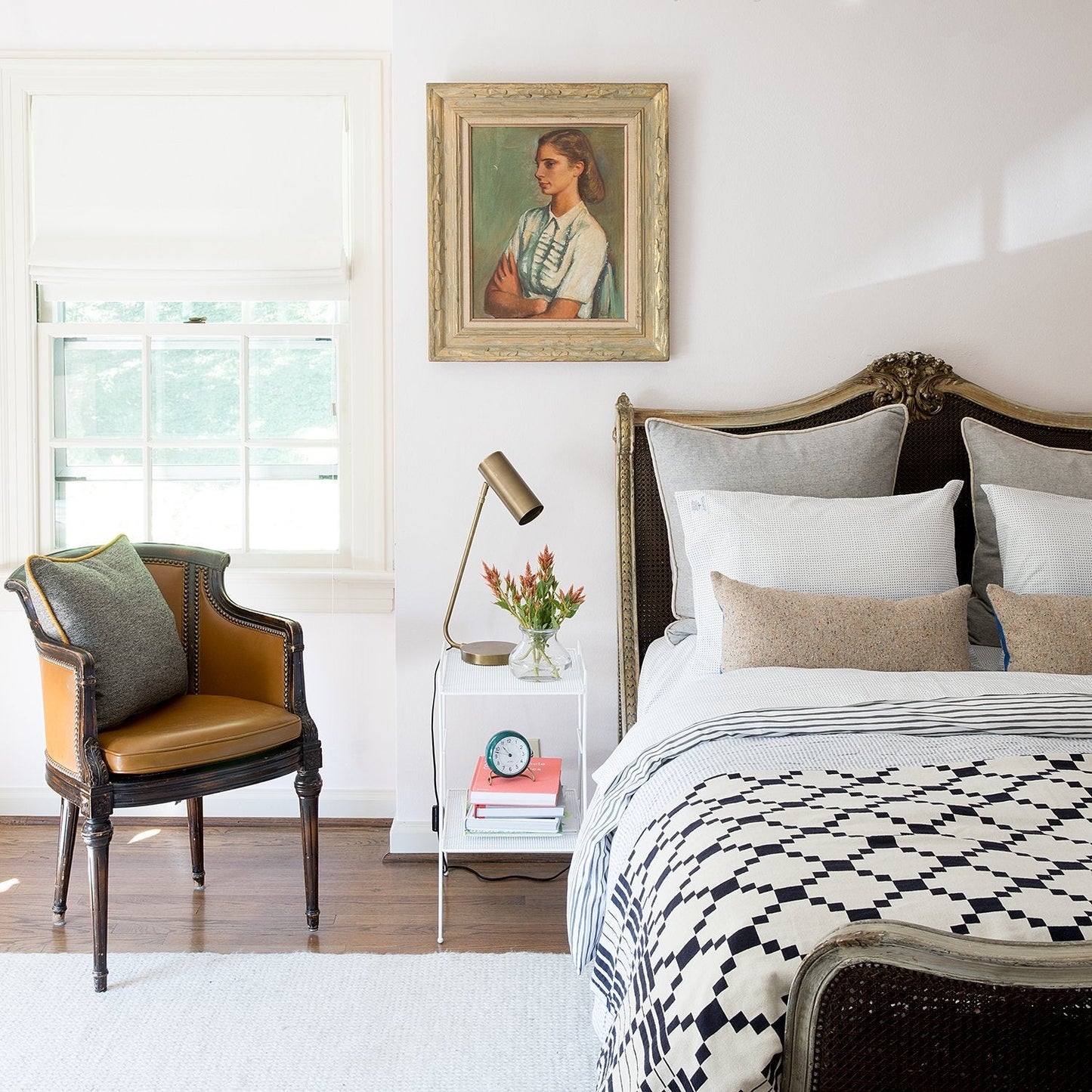 Sunlit bedroom with navy-and-white geometric coverlet on carved wood bed, bedside lamp and leather armchair