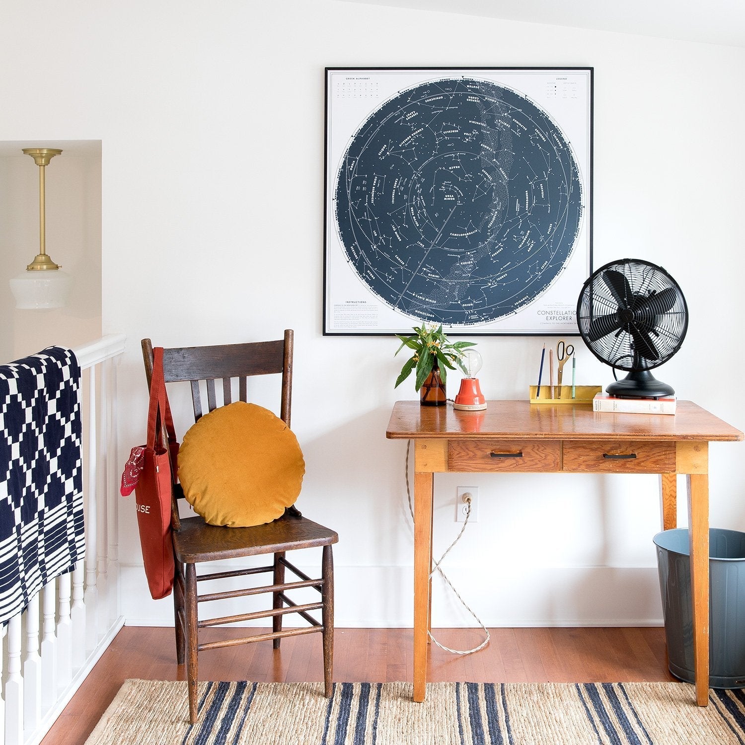 Winter and Summer cotton coverlet in navy and white draped over a stair railing beside a wooden chair and a wooden desk in a bright styled room