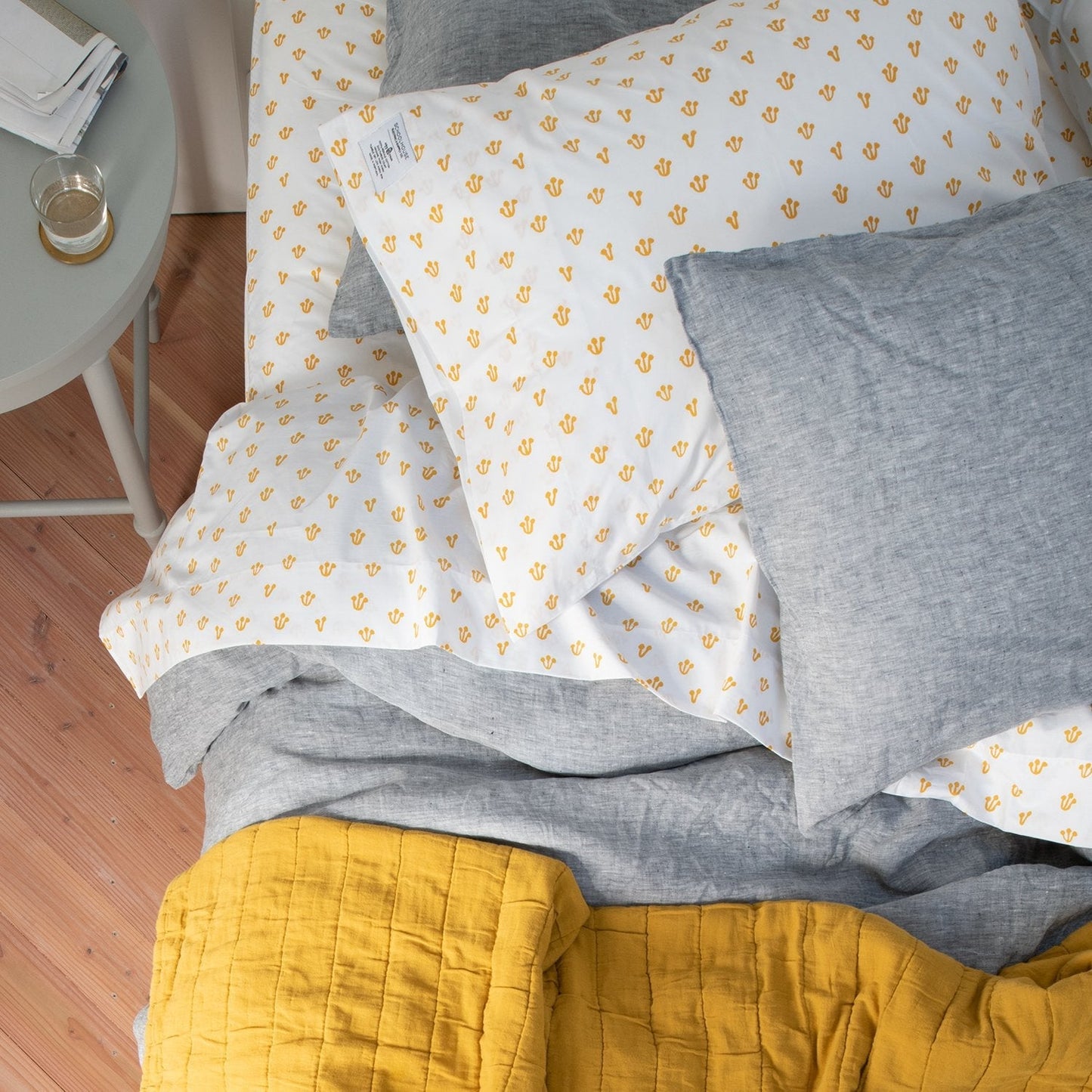 Top view of Thistle Percale Sheet Set showing yellow thistle print on white percale with gray linen and mustard quilt