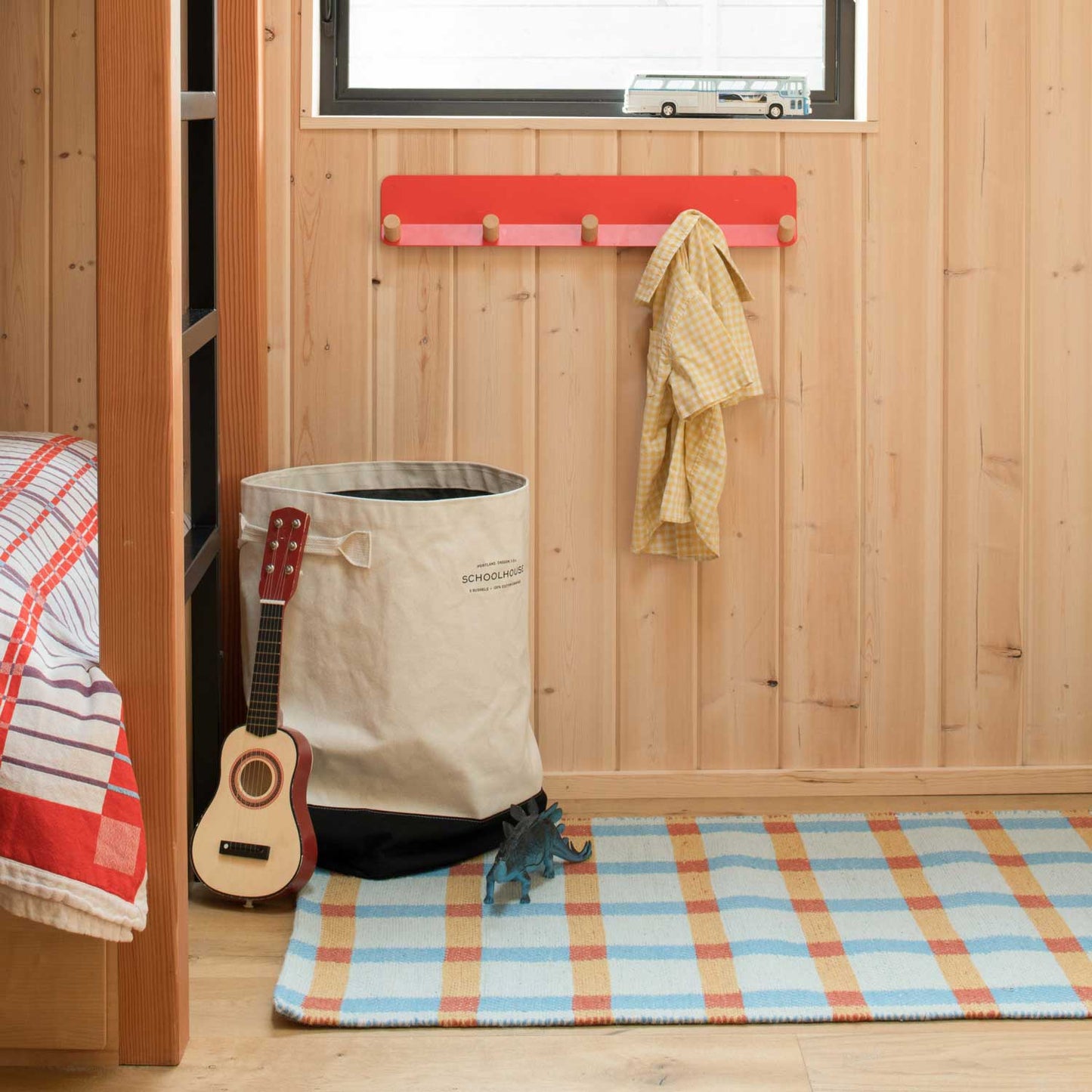 Plaid wool rug on hardwood floor in a child’s room with a canvas storage bin, toy ukulele, and wooden peg rack