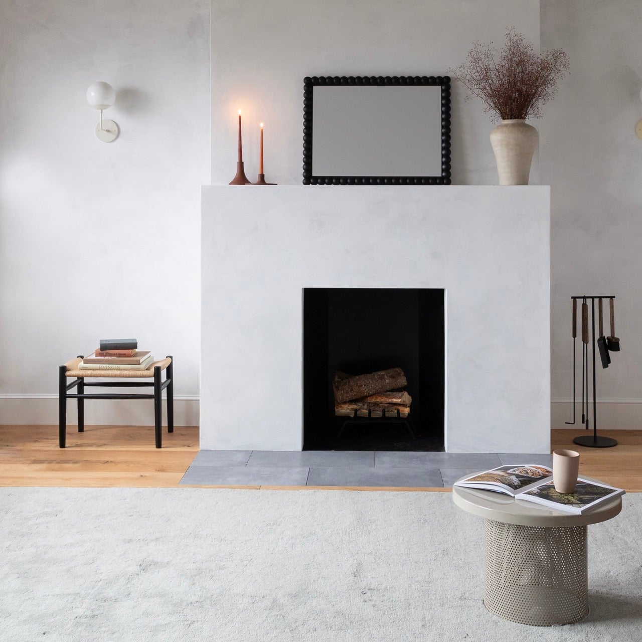 Bobbin mirror leaning on a white mantel in a minimalist living room with lit candles and a ceramic vase
