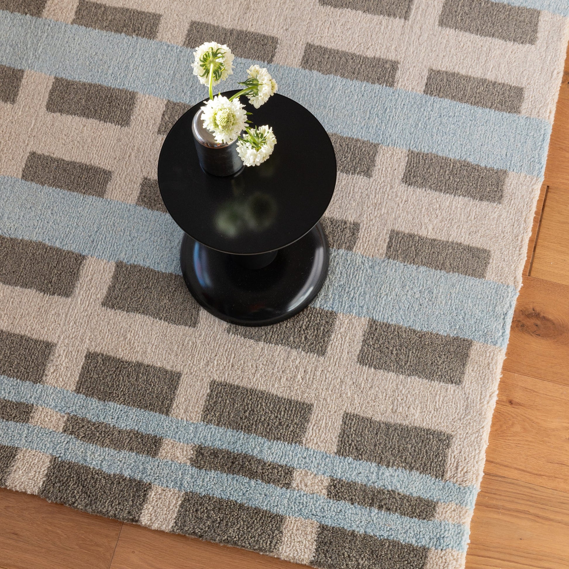 Overhead view of Network Tufted Wool Rug, plush blue-and-gray geometric blocks, styled with a black side table