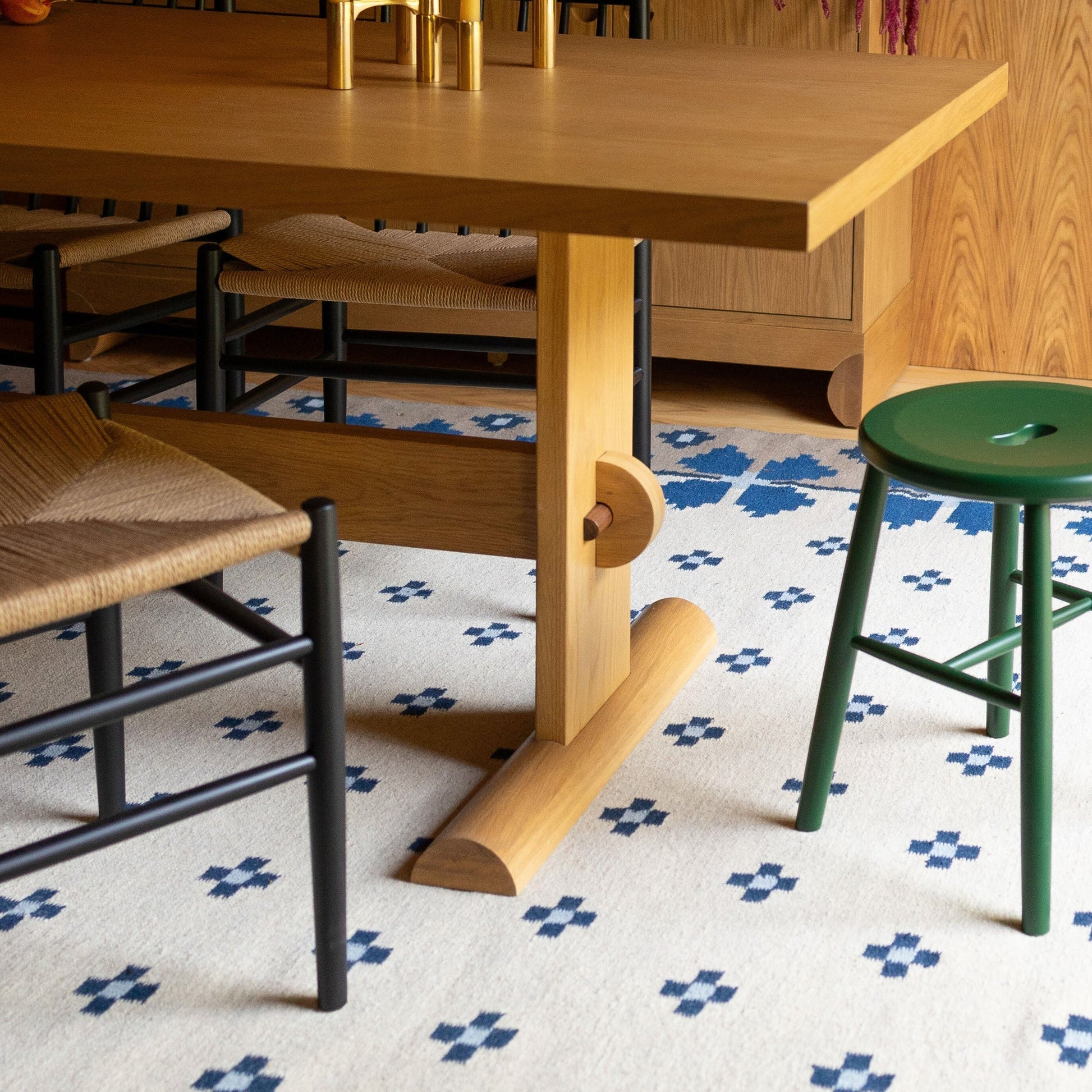 Close-up of Flora Wool Flatweave Rug showing blue folk floral motifs on a cream flatweave wool ground under a wooden dining table and woven chairs