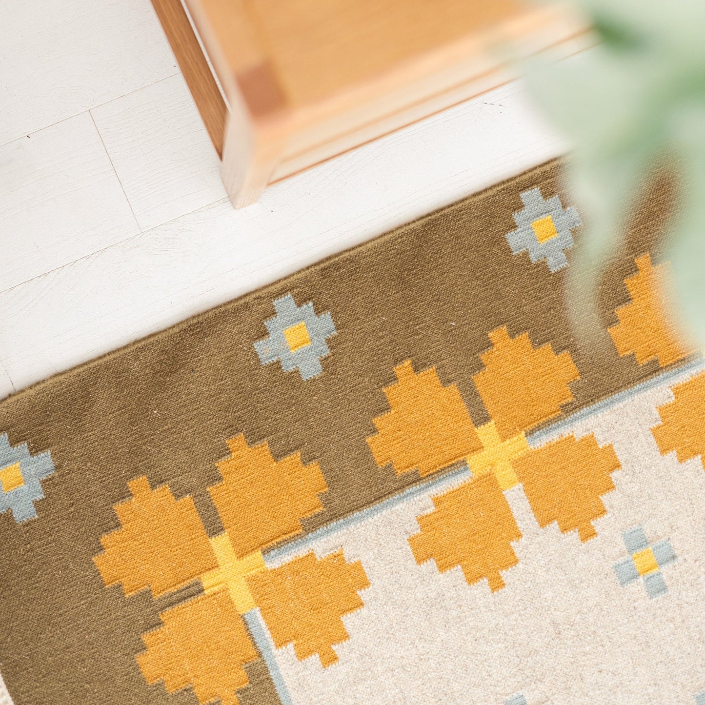 Overhead close-up of Flora Wool Flatweave Rug showing wool weave and mustard-and-blue floral motif on white wood floor