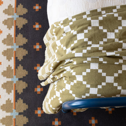 Overhead view of Flora Wool Flatweave Rug showing geometric folk-floral pattern and flatwoven texture with bed and chair