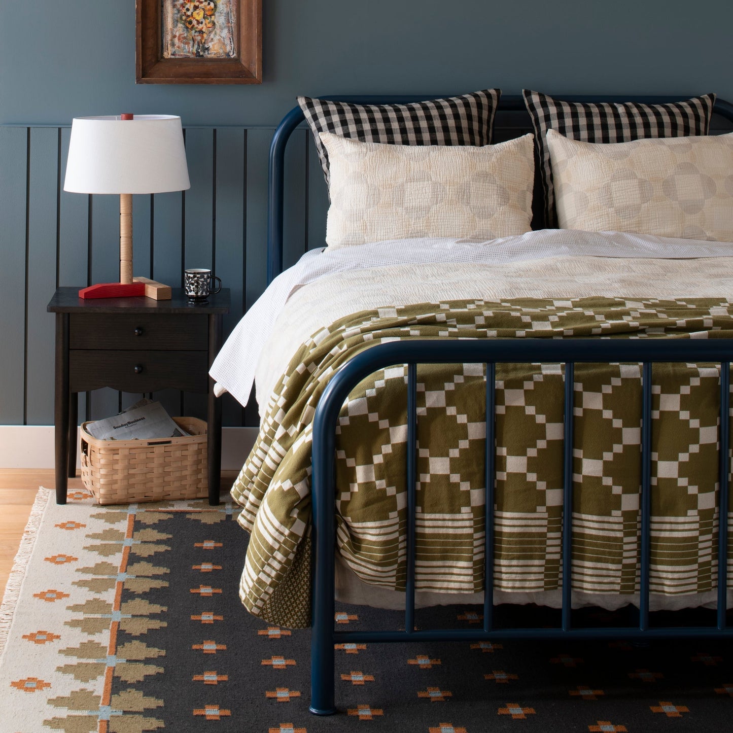 Flora Wool Flatweave Rug placed under a navy metal bed in a styled bedroom with a wooden nightstand and table lamp