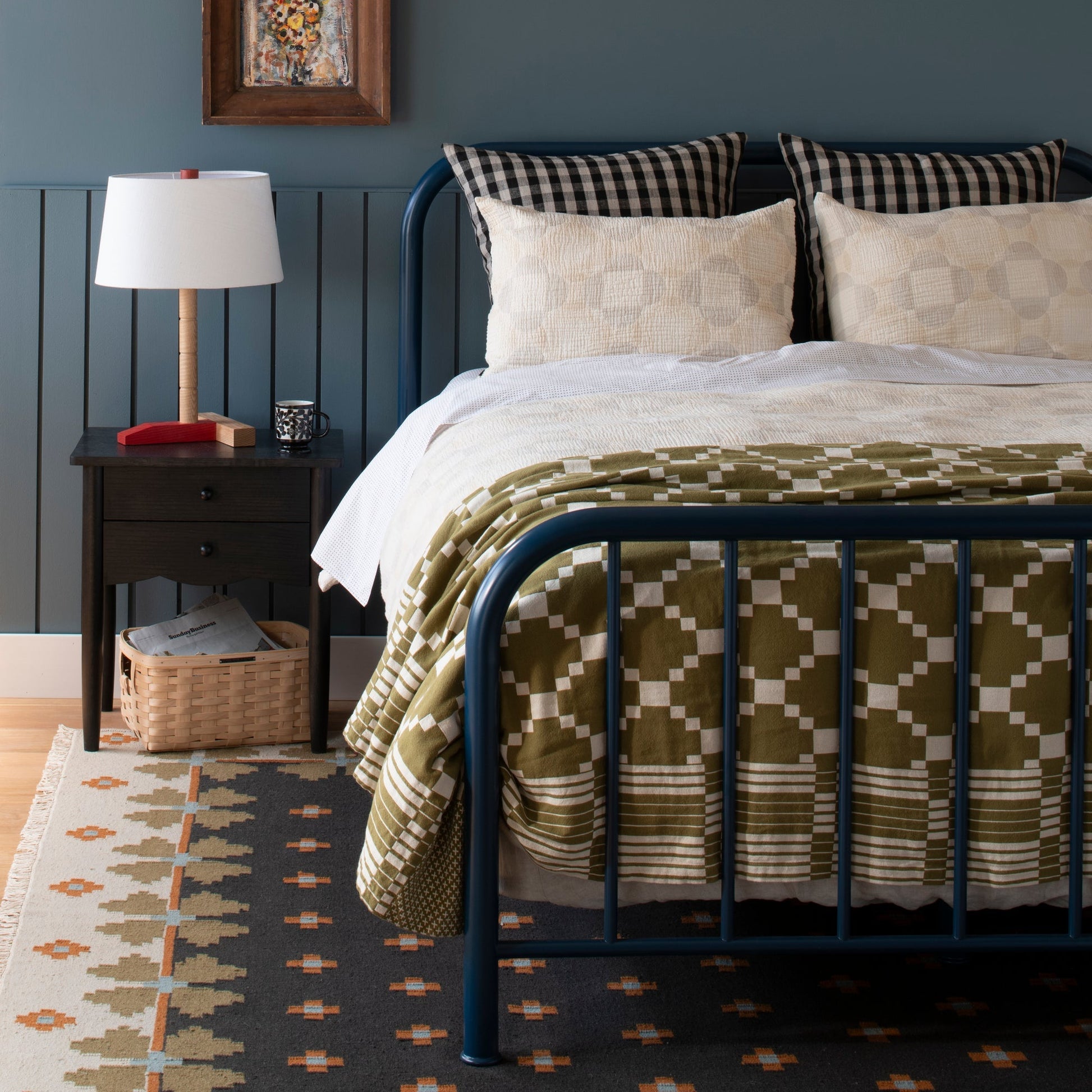 Flora Wool Flatweave Rug placed under a navy metal bed in a styled bedroom with a wooden nightstand and table lamp