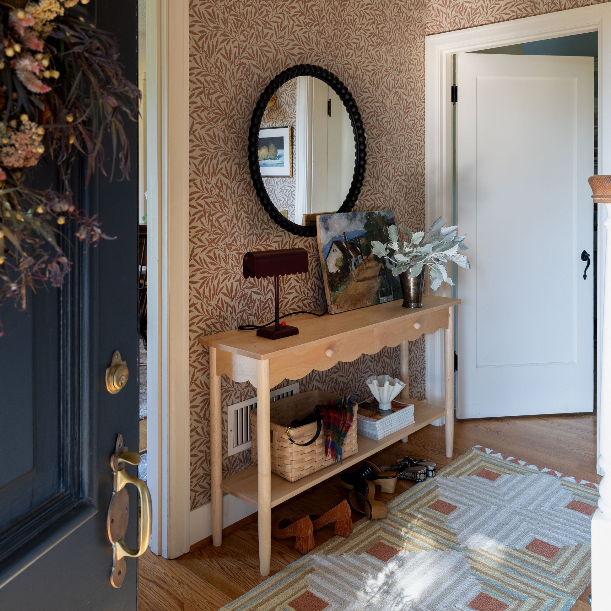 Front view of Bobbin Mirror showcasing its round beaded frame and mirrored glass on a patterned wallpapered entryway