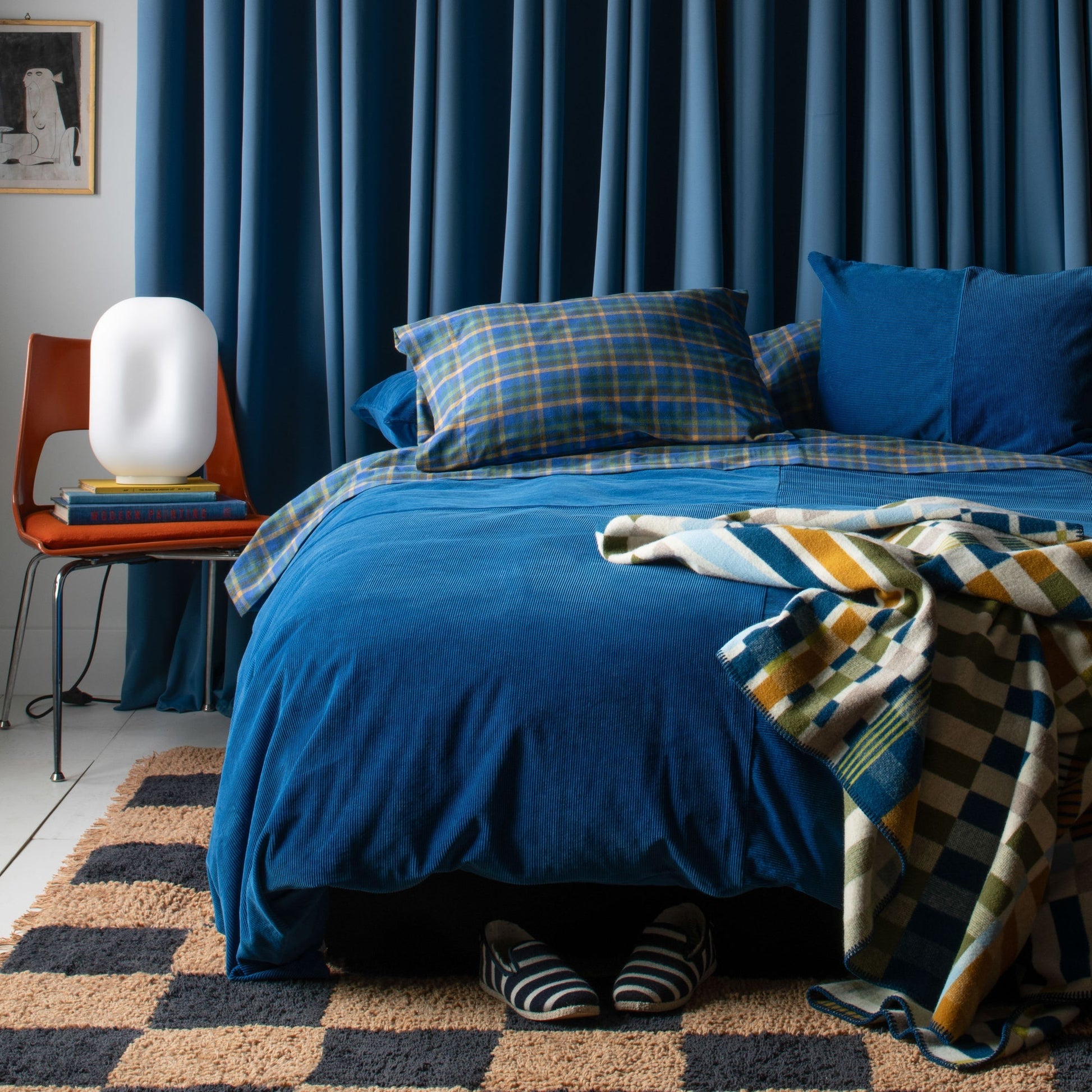 Blue-bedded bedroom with cream-and-navy checked Jacques Shag wool rug at foot of bed