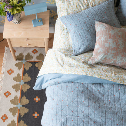 Top-down view of Wallowa Floral Percale Sheet Set with yellow floral print on cotton percale with blue quilt and nightstand