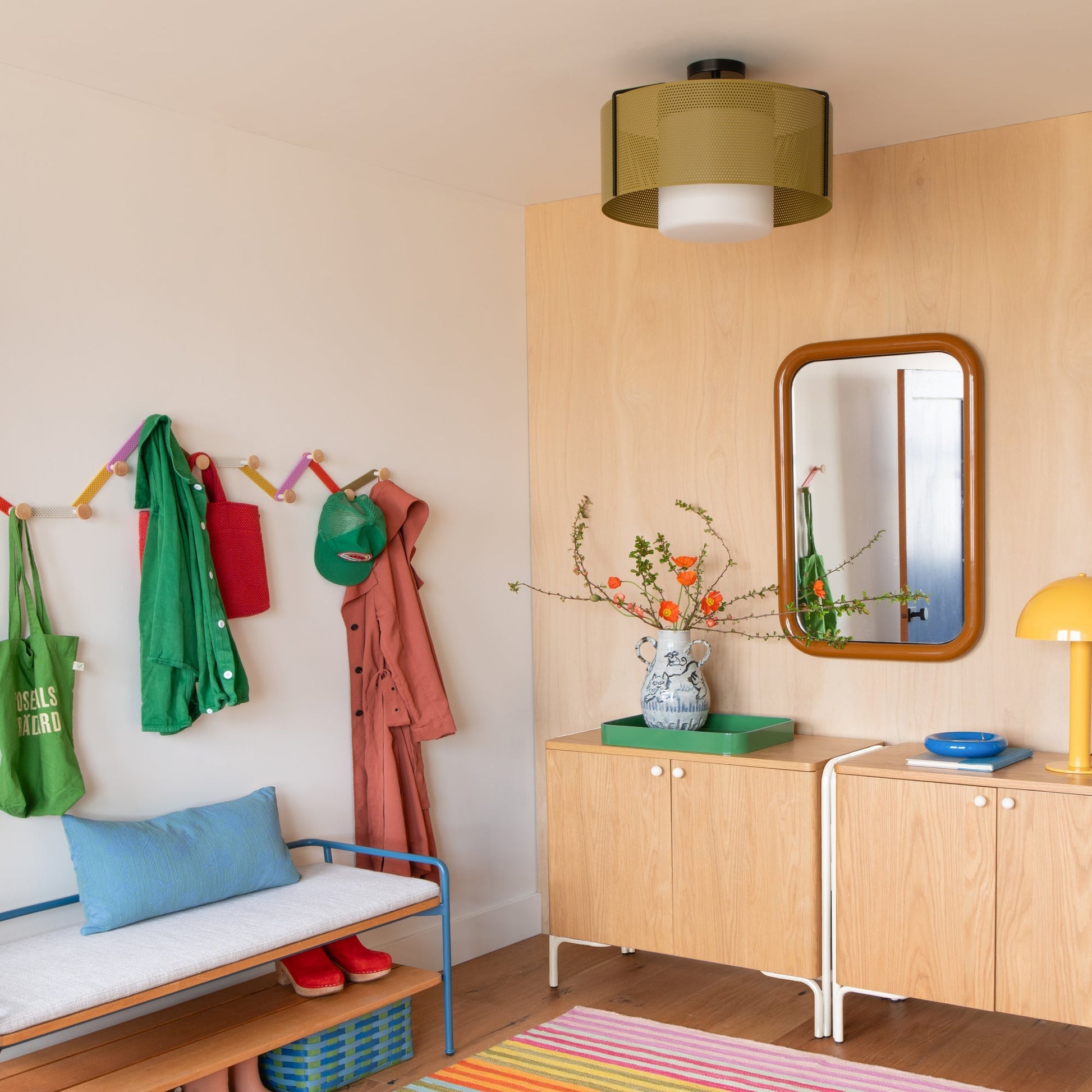 Colorful striped Lisse Performance Rug on an entryway floor beside a wood cabinet, mirror, bench, and wall hooks