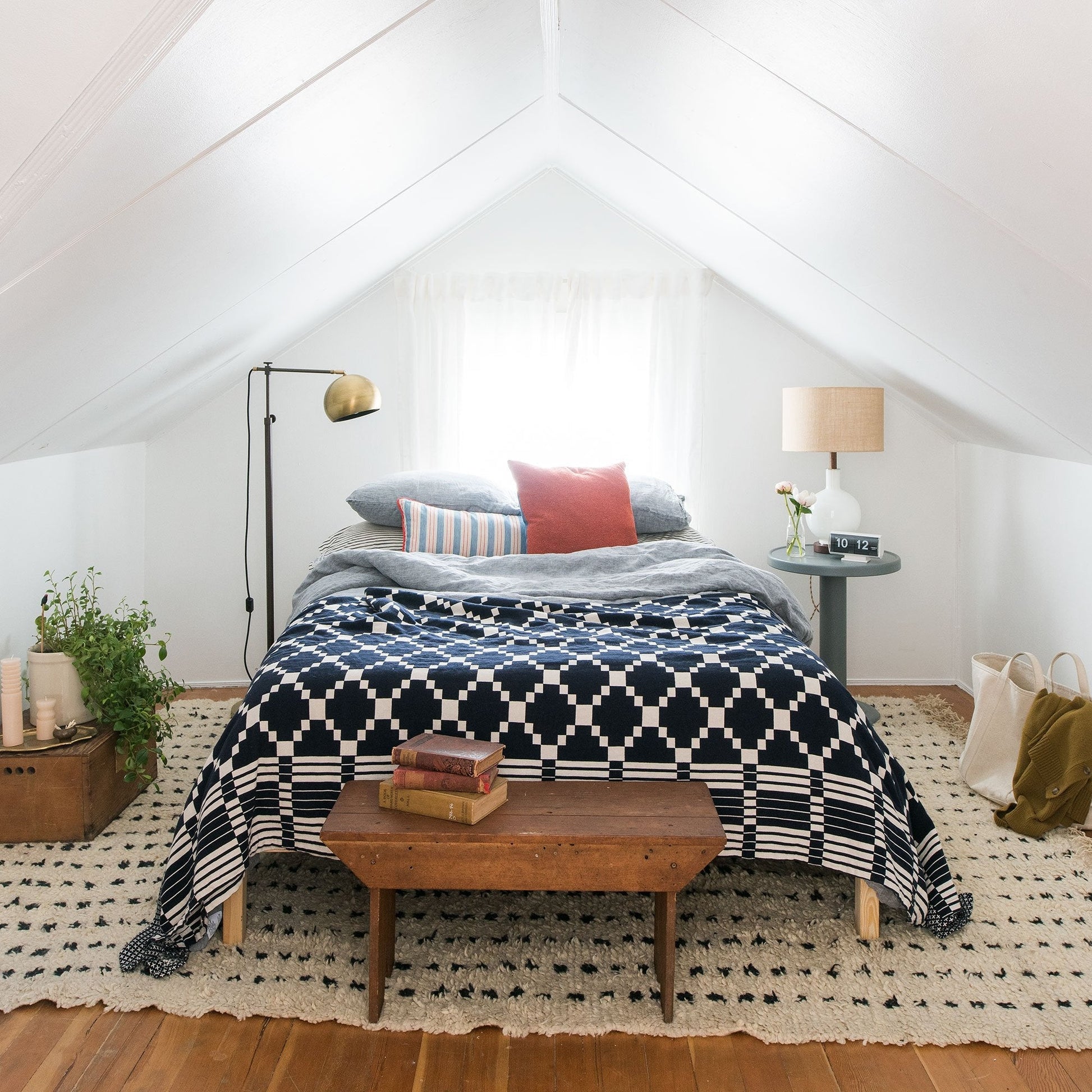 Bed styled with Winter + Summer cotton coverlet (navy geometric) layered with pillows in a bright airy attic bedroom