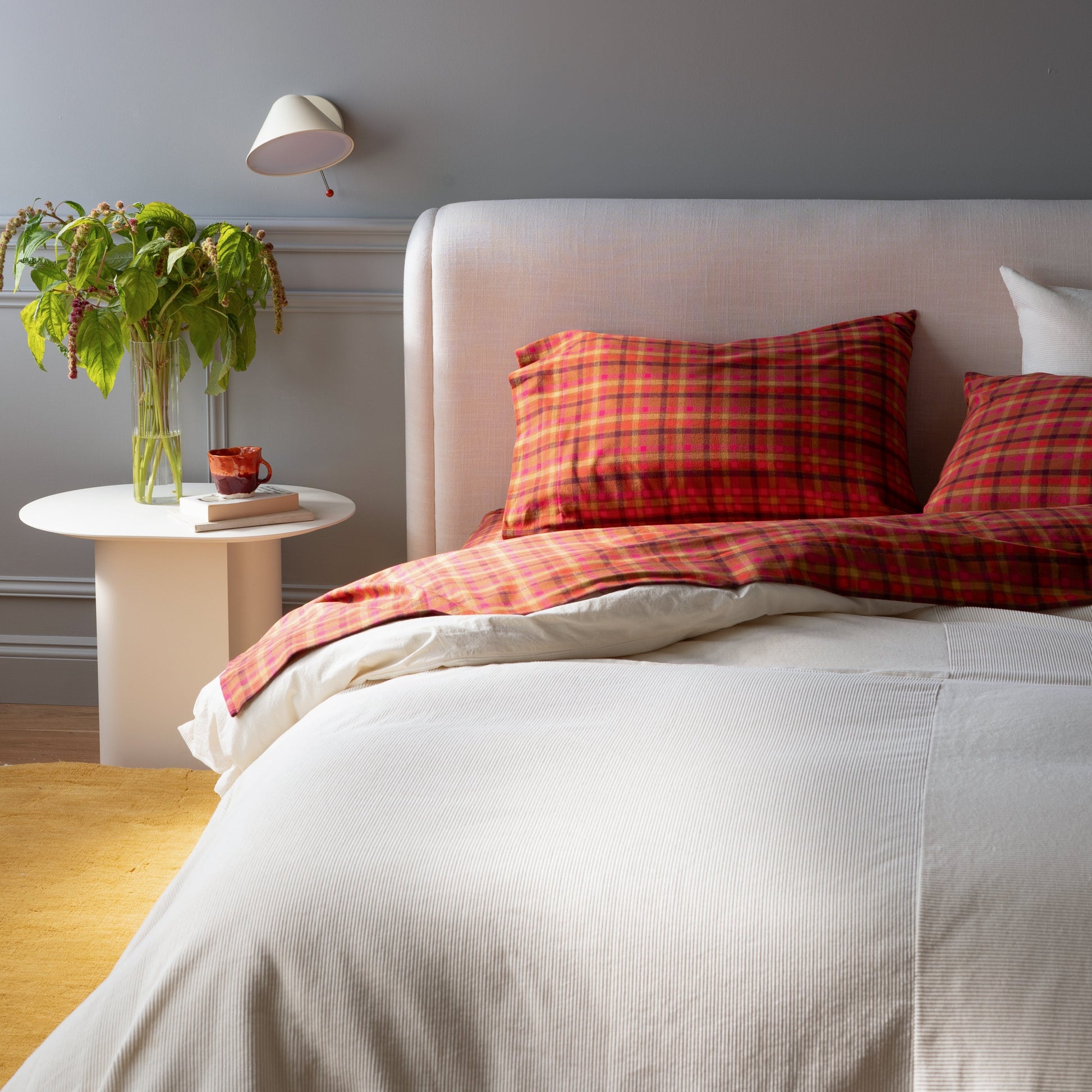 Bedroom styled with Mesa Wool Rug under bed, upholstered pink headboard, red plaid pillows, side table with vase and wall sconce