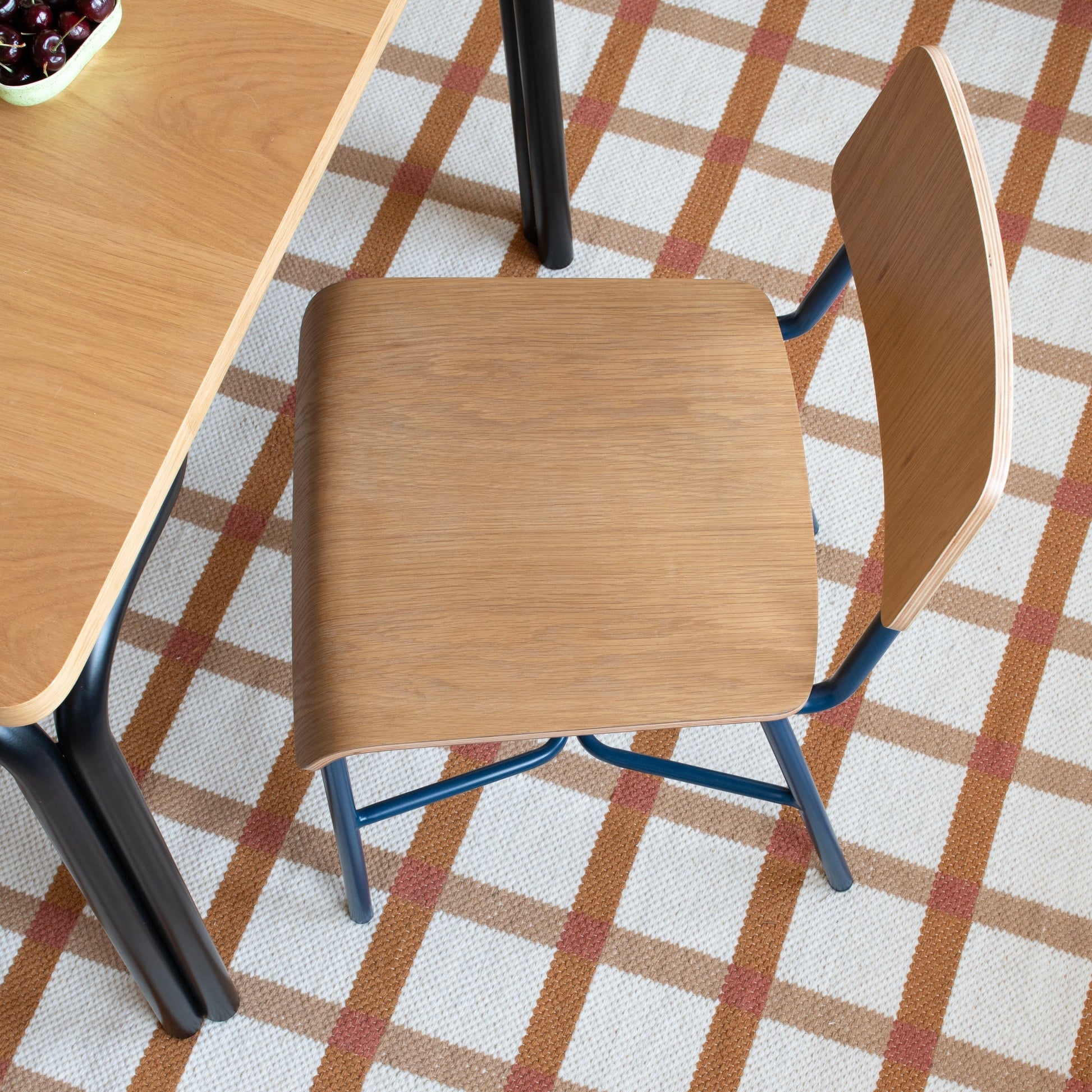 Top-down view of Plaid Wool Reversible Rug showing tan and rust plaid on white woven wool under a wooden chair and table
