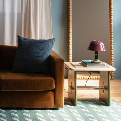 Angled view of Bobbin Mirror showcasing its beaded ash wood frame with a brown sofa, navy pillow, and side table lamp